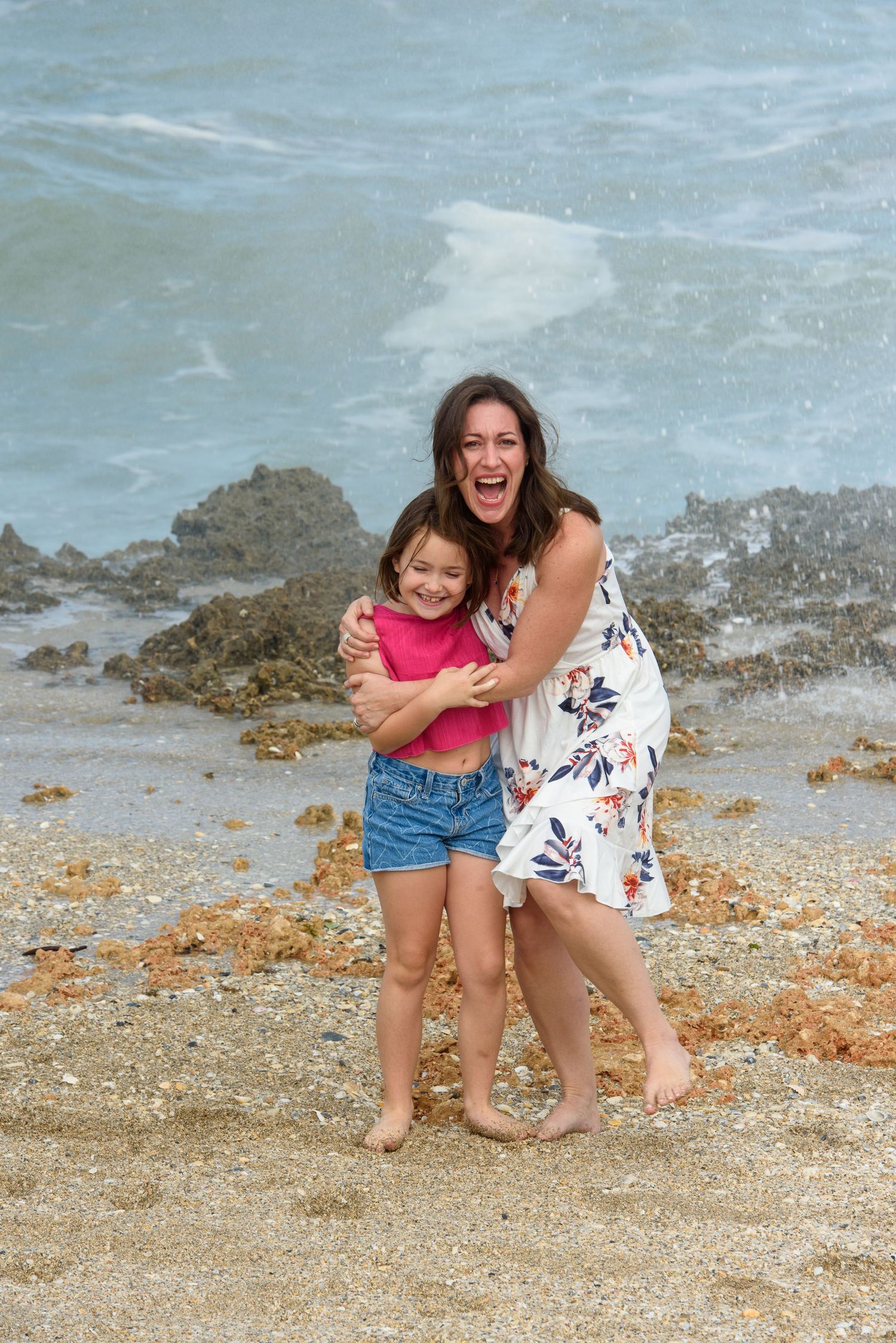 Two people enjoying a playful moment on a beach with waves crashing against rocks.