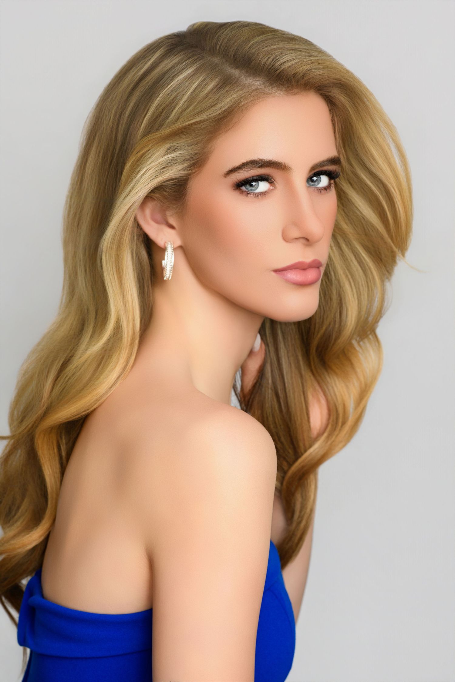 Portrait of a woman with wavy blonde hair wearing a royal blue strapless top against a light gray background.