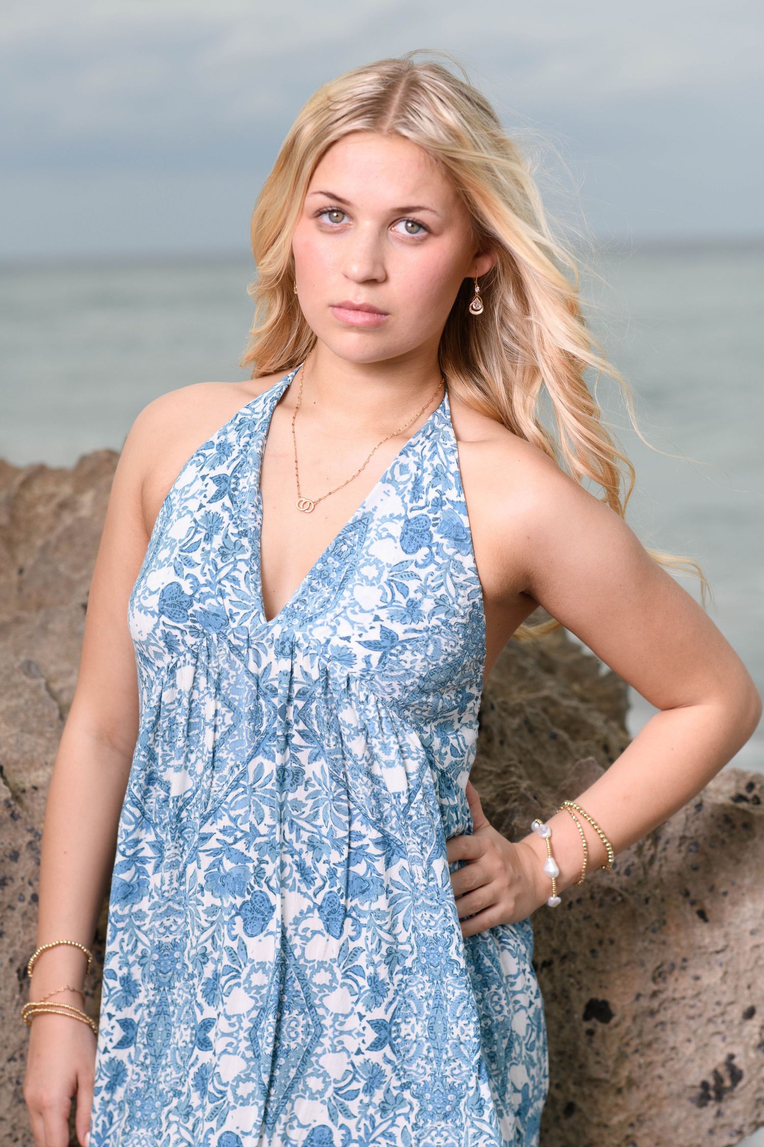 A blue and white floral sundress is showcased in multiple poses along a beachside rock formation.