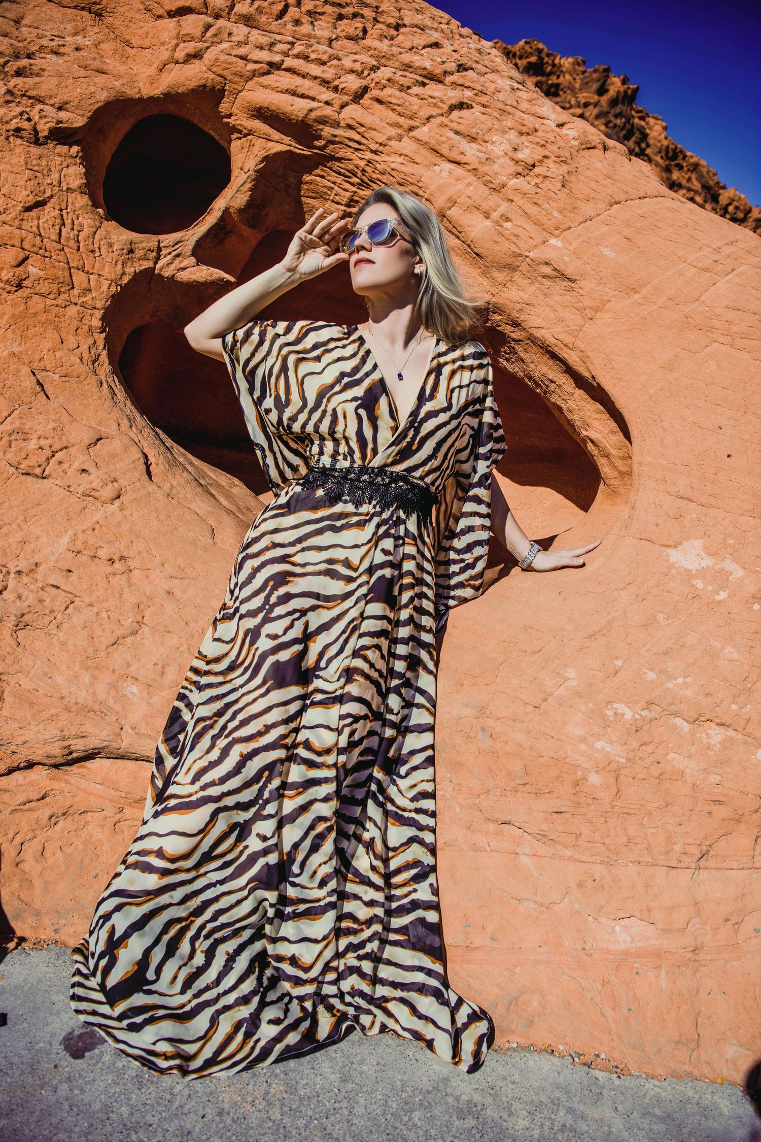 Fashion shot of model in zebra print maxi dress against red rock formation. Destination fashion shoot in the Nevada Valley of Fire