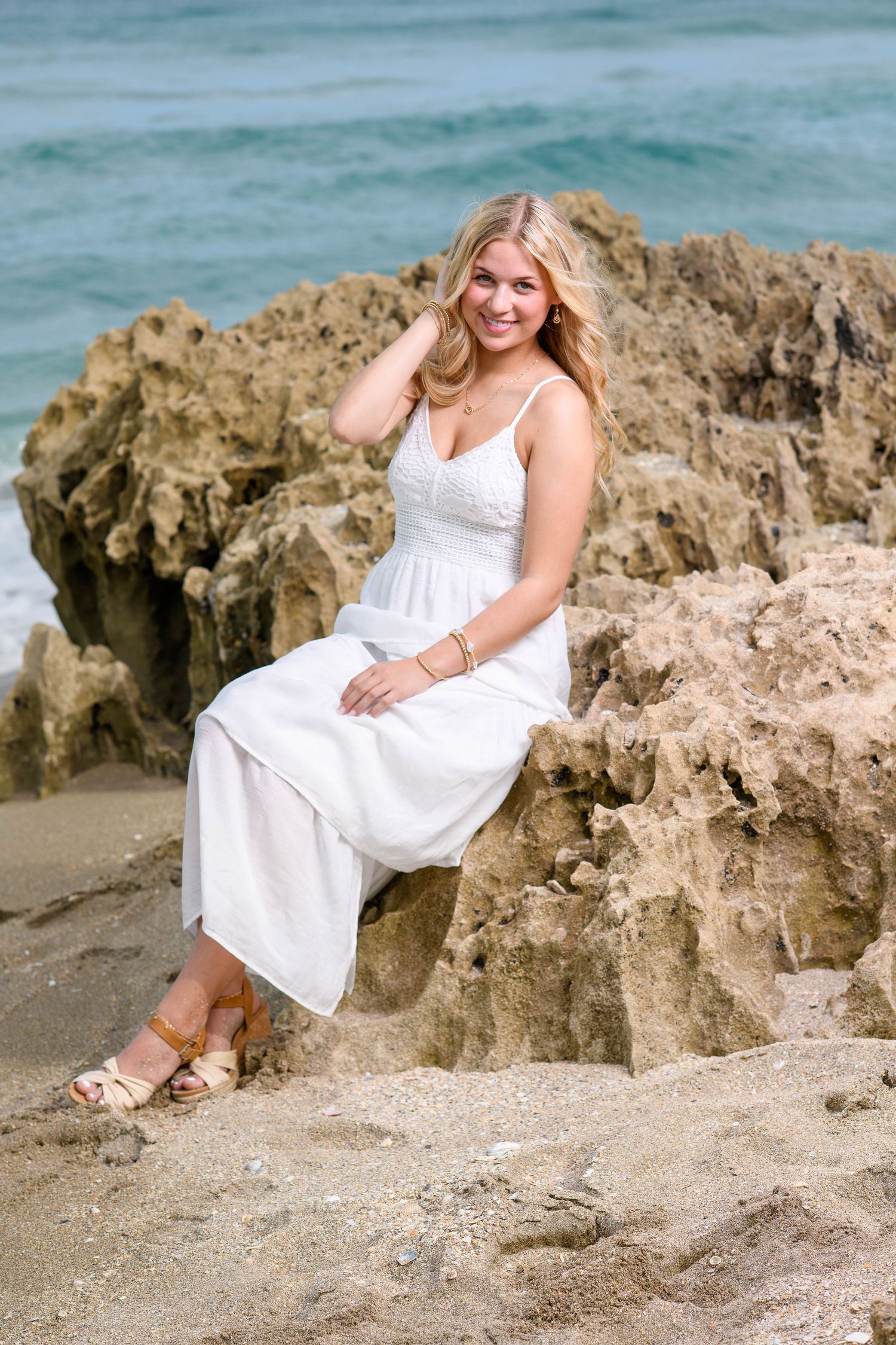 A white sundress photoshoot on a rocky beach with turquoise waters and limestone formations in the background.