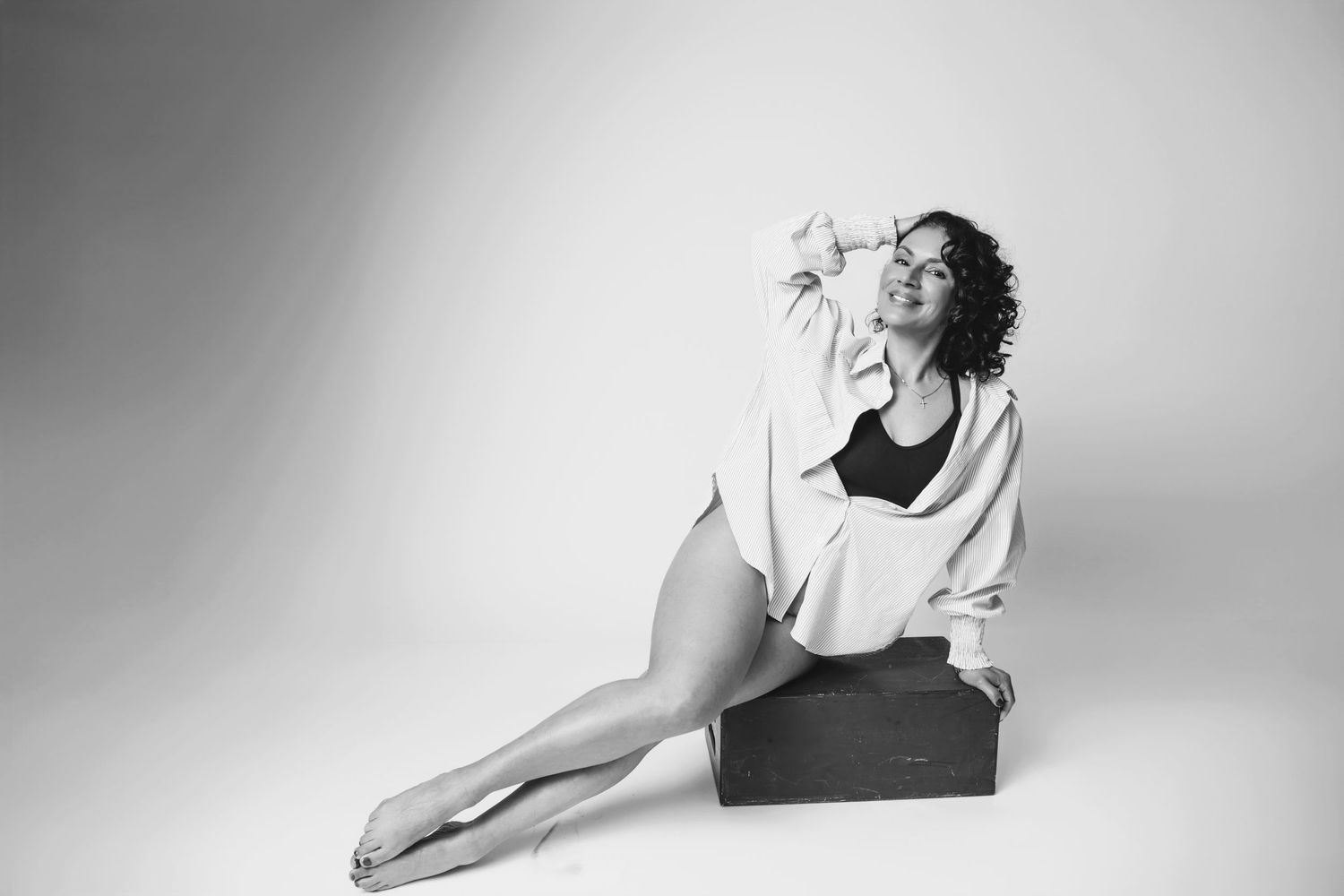 Black and white portrait of model in athletic wear and white cardigan posing on box in studio setting.