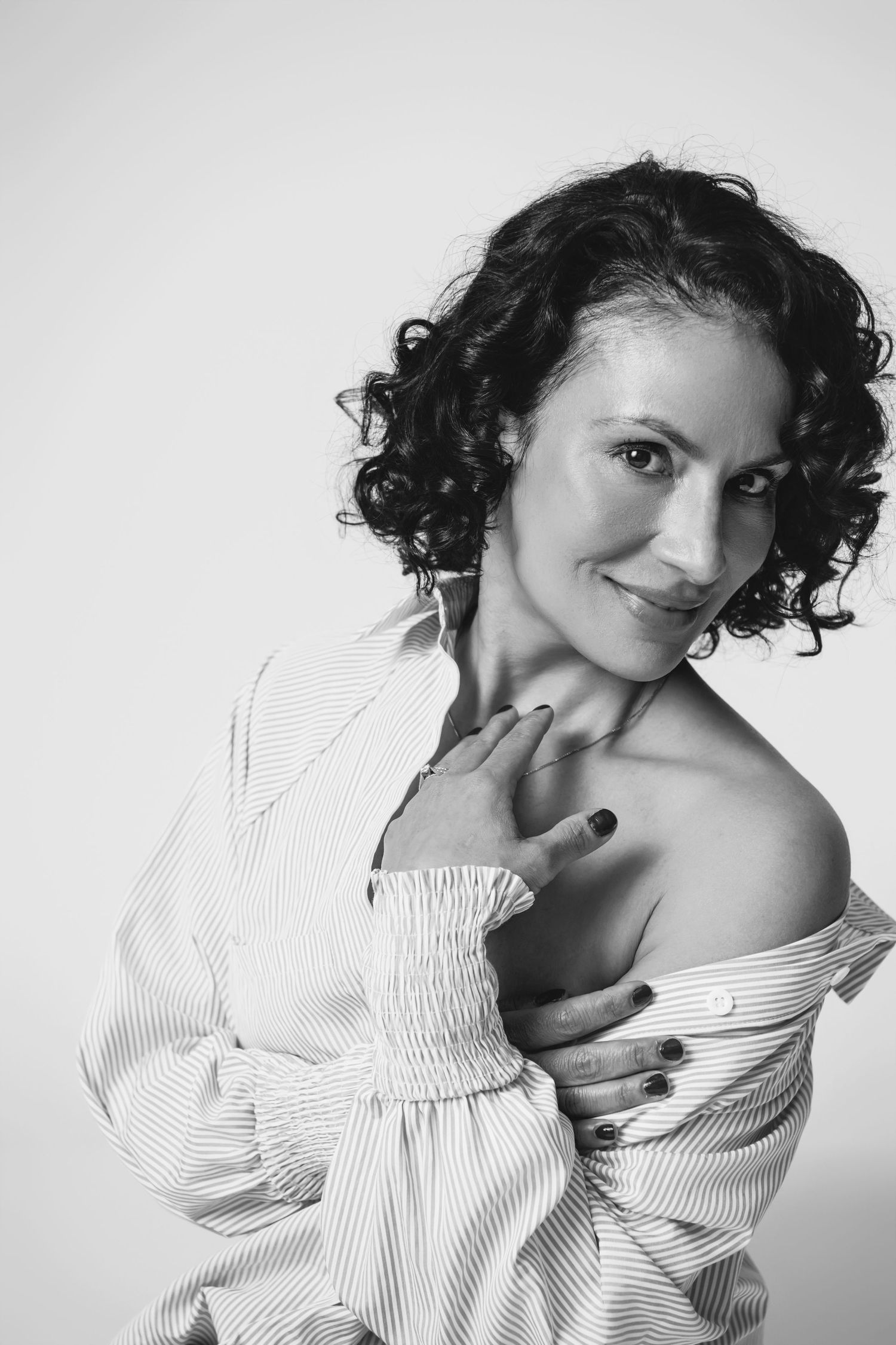 Close-up portrait in striped off-shoulder top showing natural curls against white backdrop.