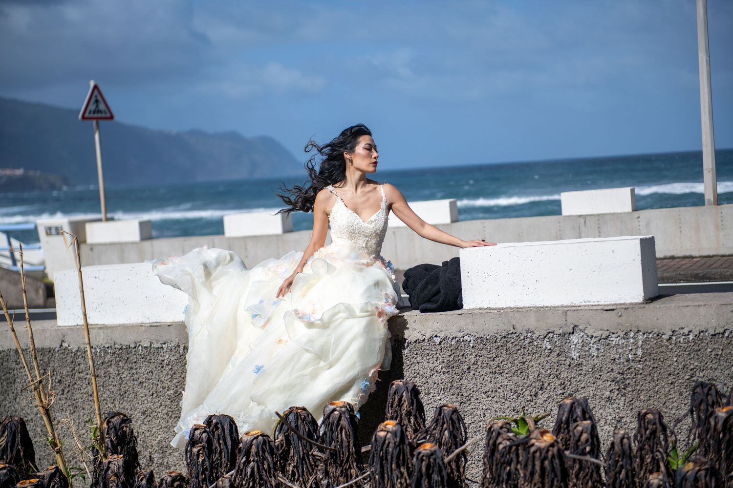 White dress flowing in the wind against a seaside wall with ocean views.