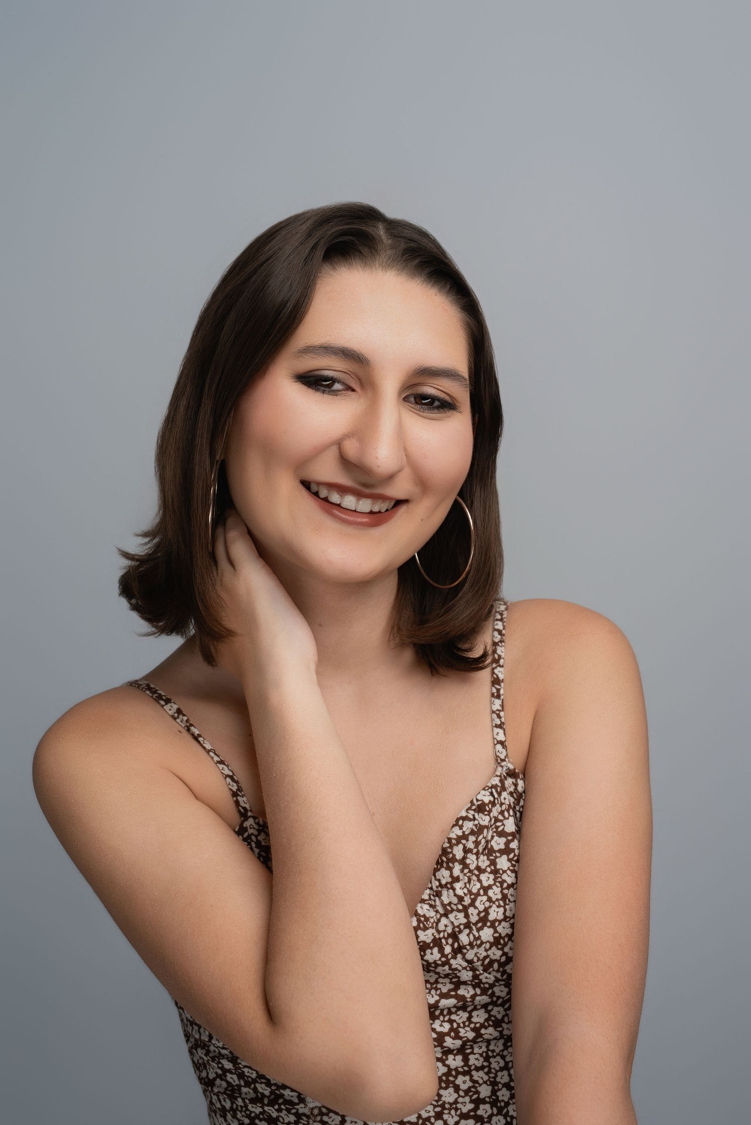 Portrait series showing high school senior in patterned top posing confidently against gray background.