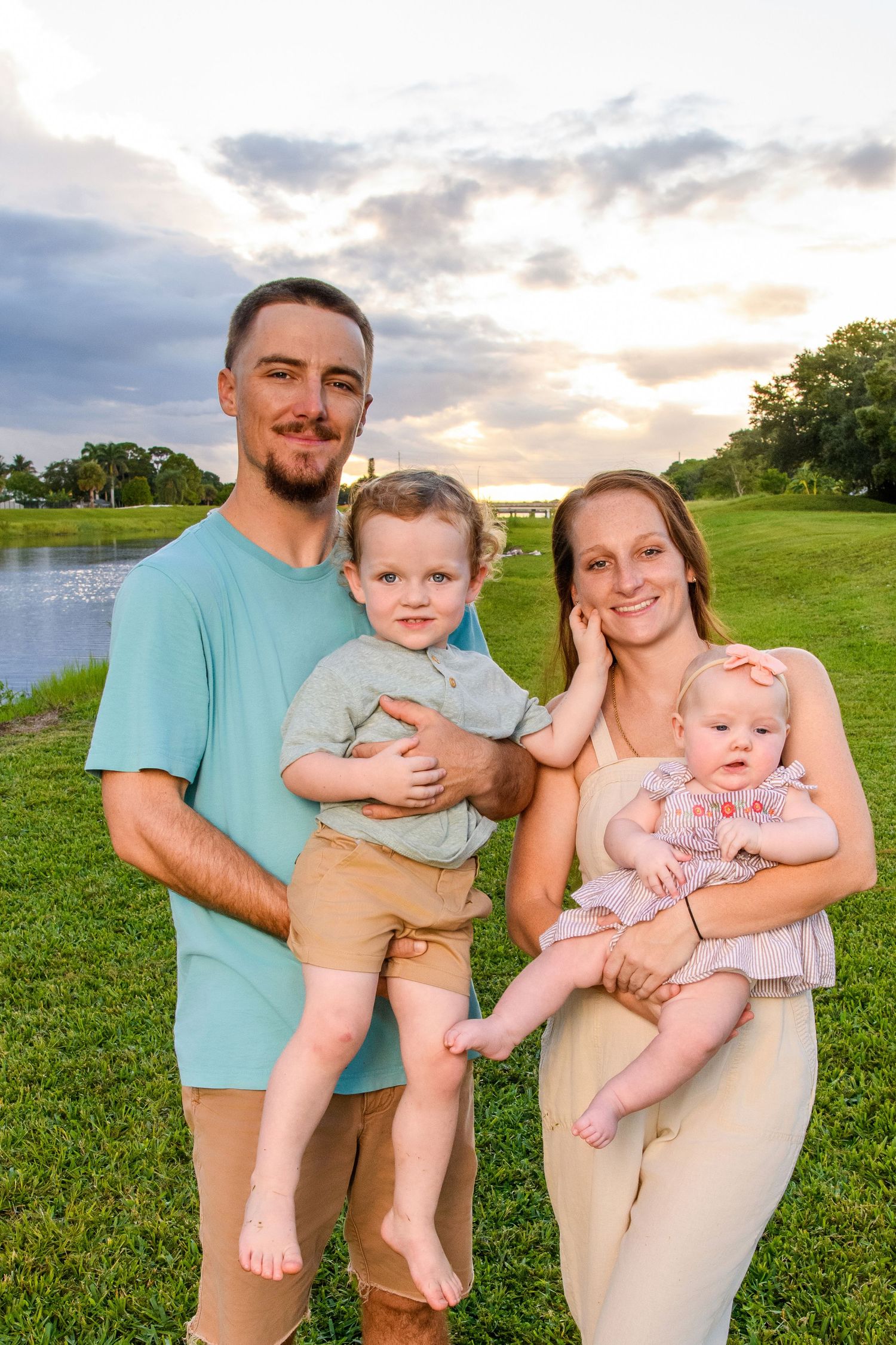 Family of four poses together on grassy hill during sunset photoshoot.