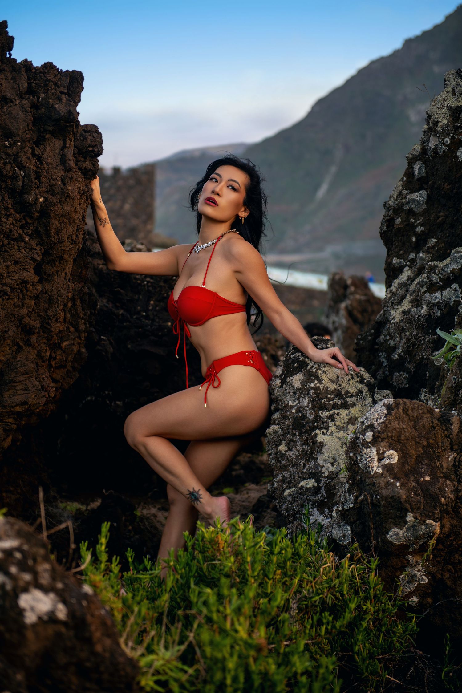 Fashion portrait on volcanic rocks showing red swimwear against dramatic coastal scenery.