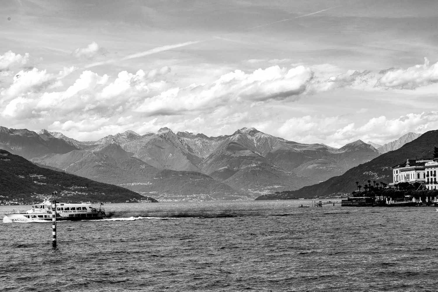 Panoramic black and white landscape of mountains and lake with cloudy sky.
