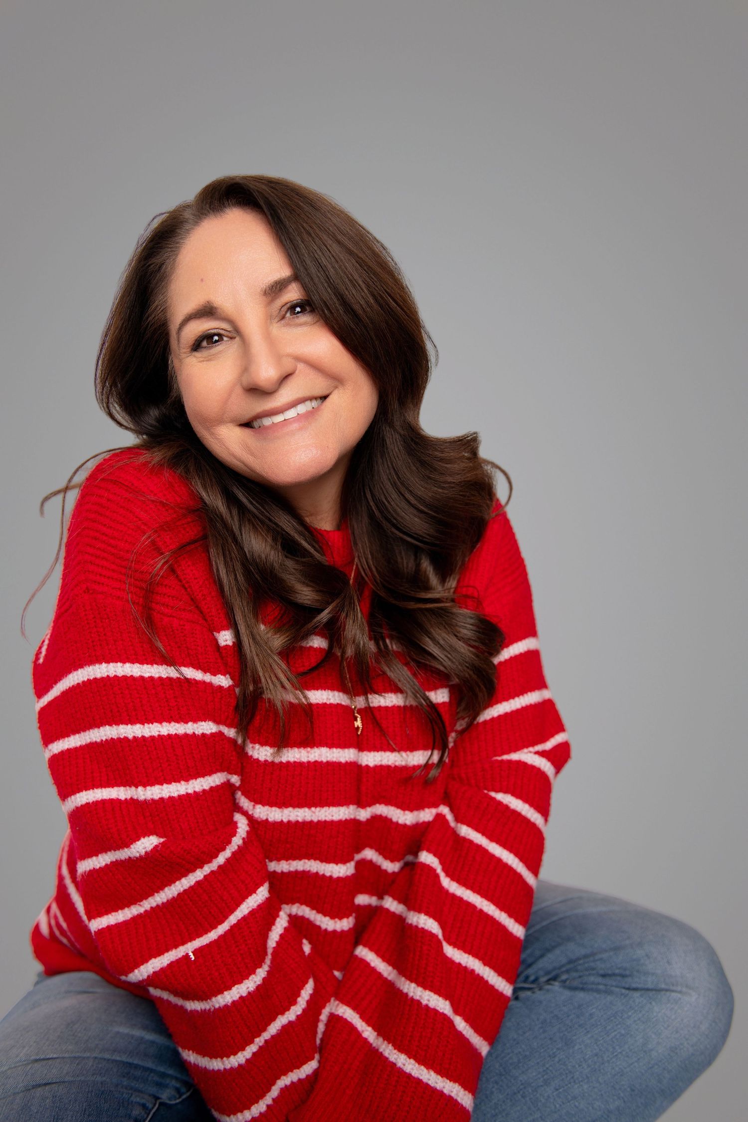 Person in red and white striped sweater poses playfully against grey background.
