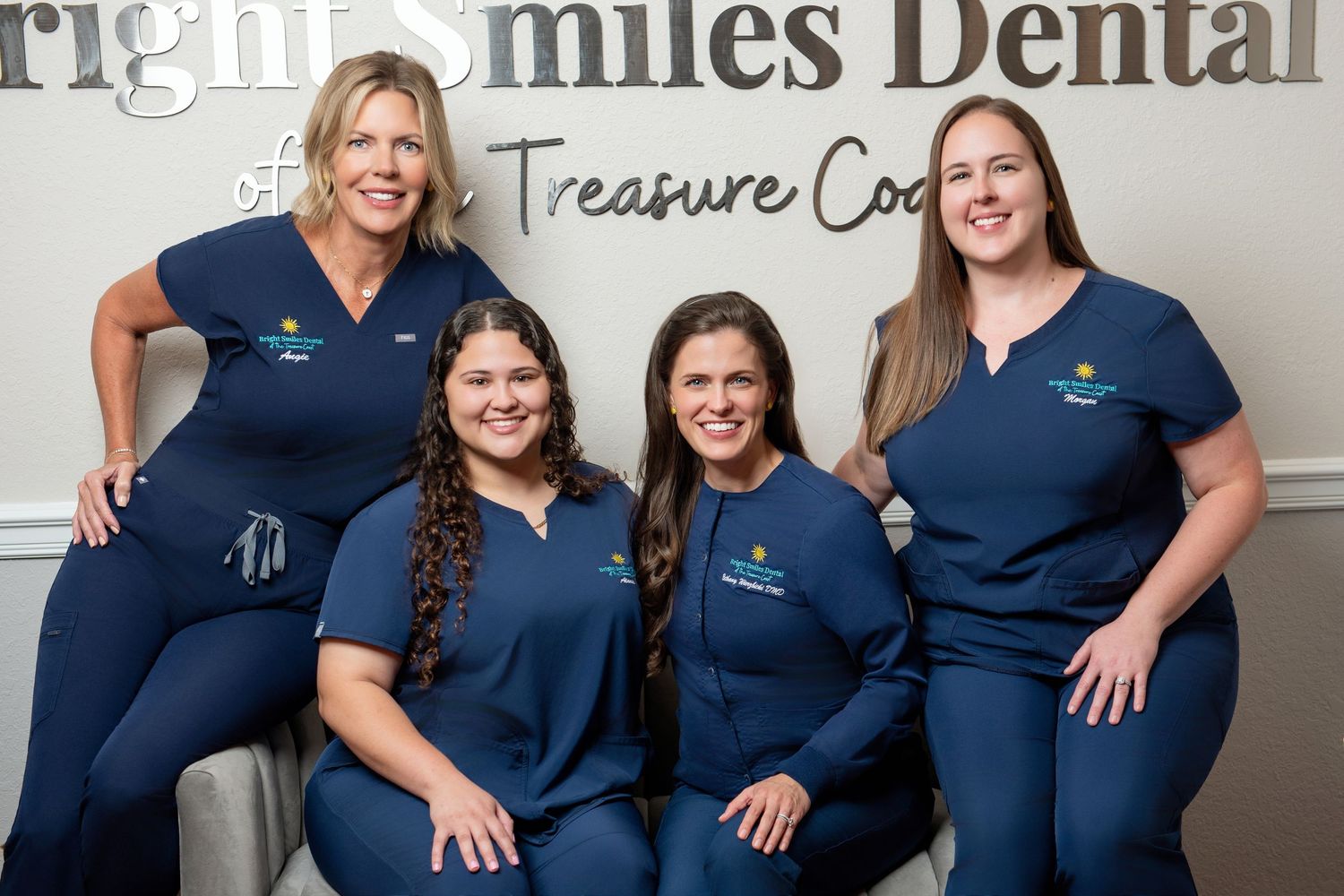 Dental office team members in navy uniforms pose together for group photo.
