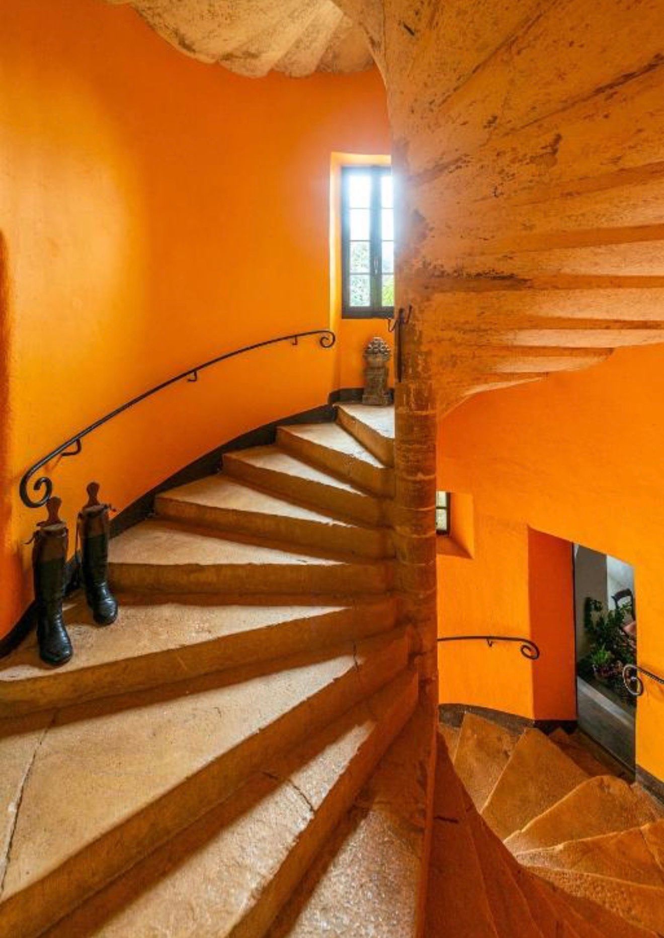 Stunning spiral staircase with vibrant orange walls and stone steps in a rustic Mediterranean-style interior.