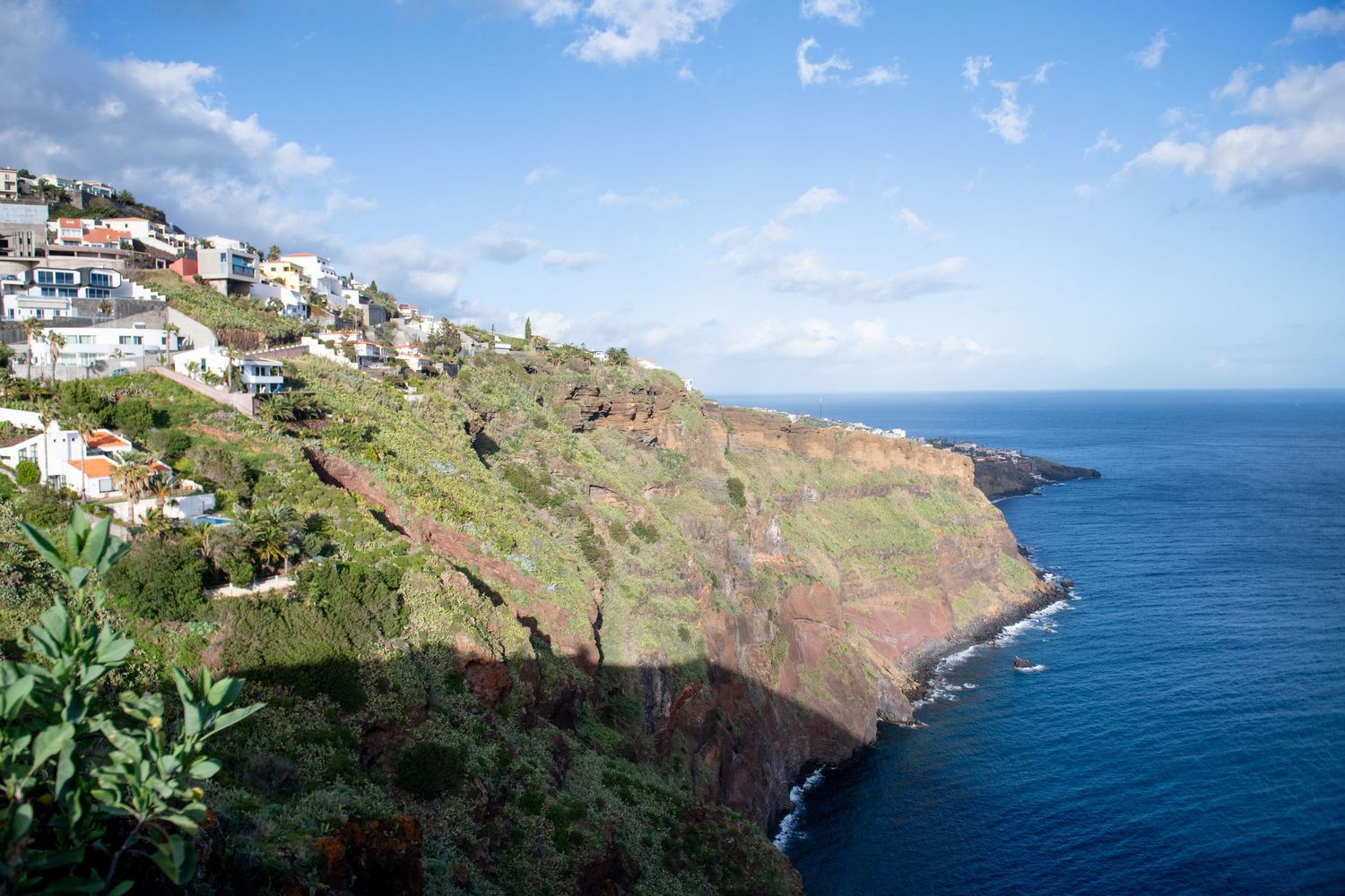 Scenic coastal view of white buildings perched on cliffs overlooking deep blue ocean waters.