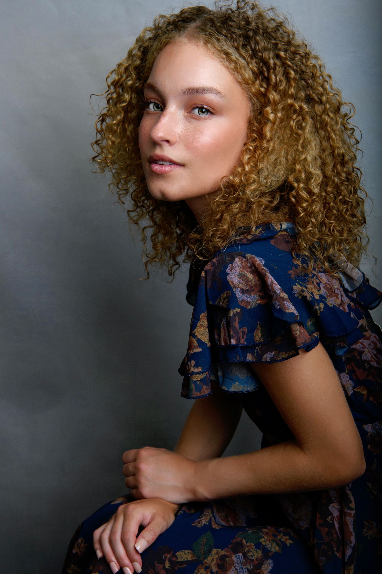 Portrait in navy floral dress with natural curly hair against grey background.