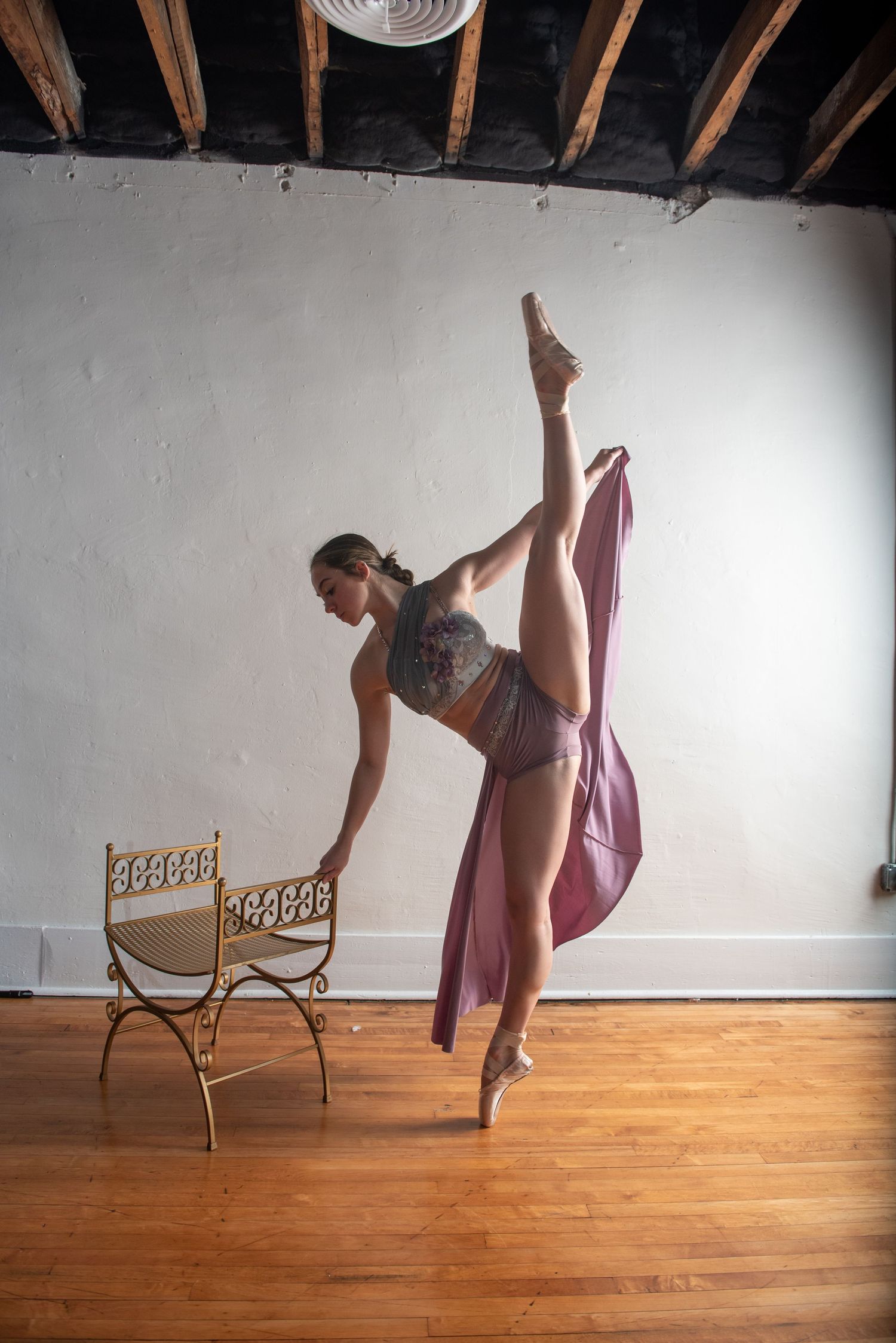 Ballet dancer performing elegant movements in a mauve dress with dramatic lighting.
