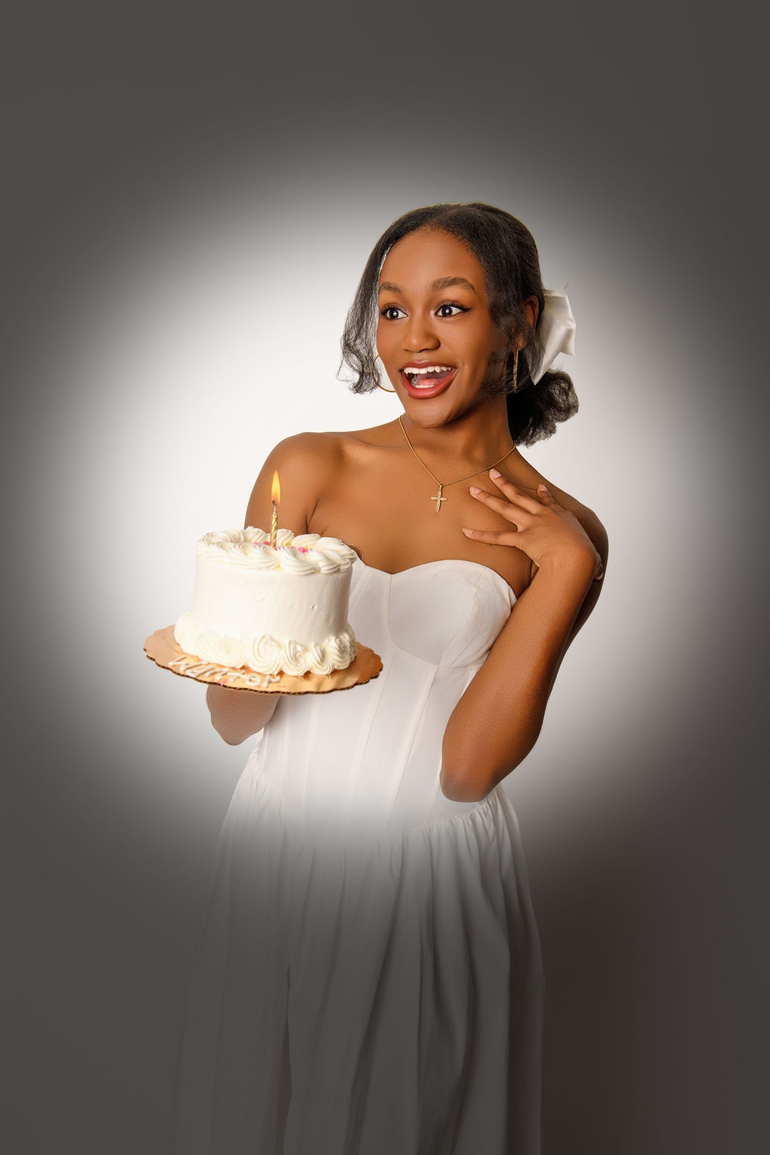 Elegant model in white dress holds decorated white cake against grey backdrop.
