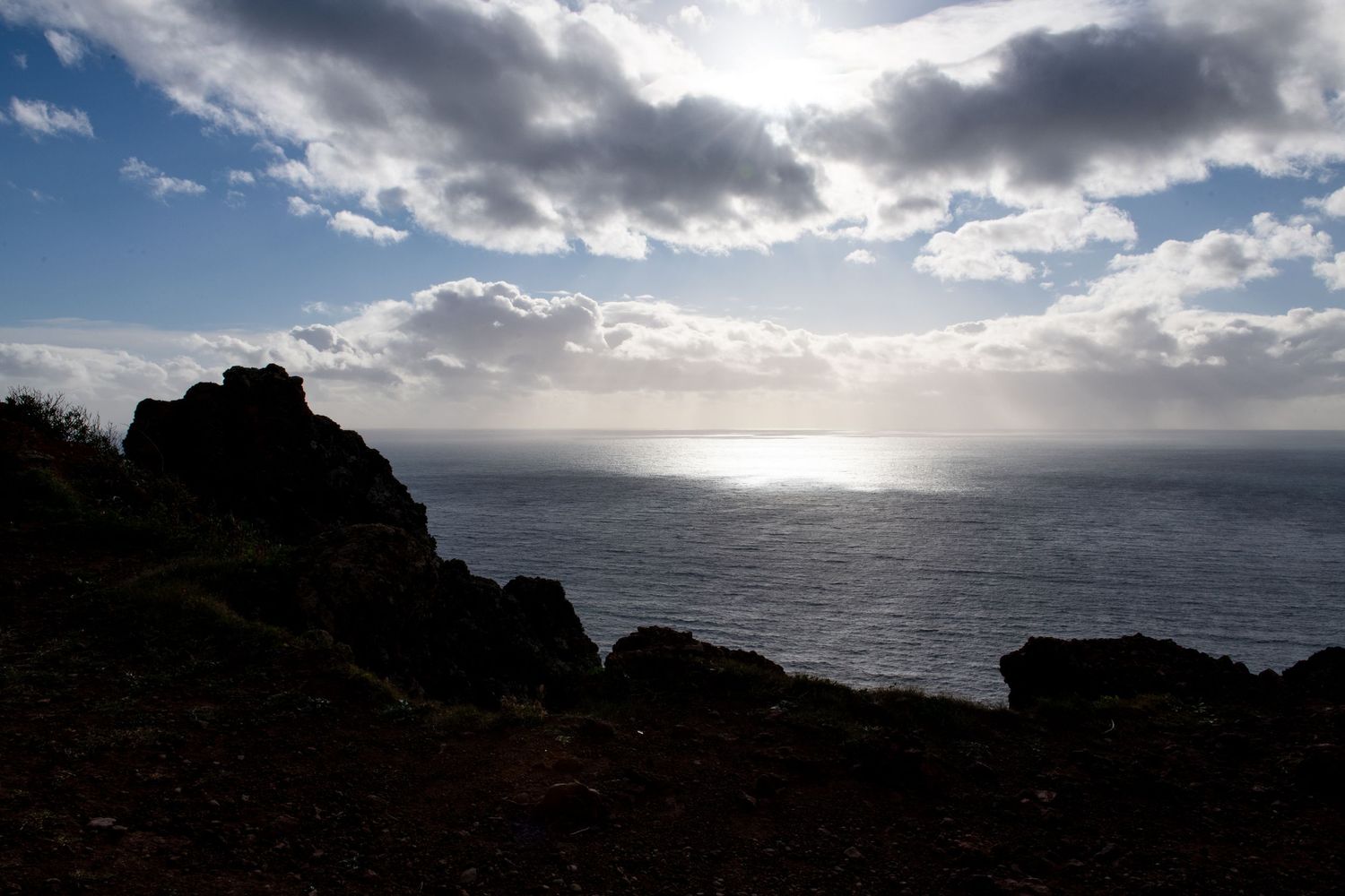 Dramatic sunset over ocean with rocky silhouettes and sunbeams breaking through clouds.