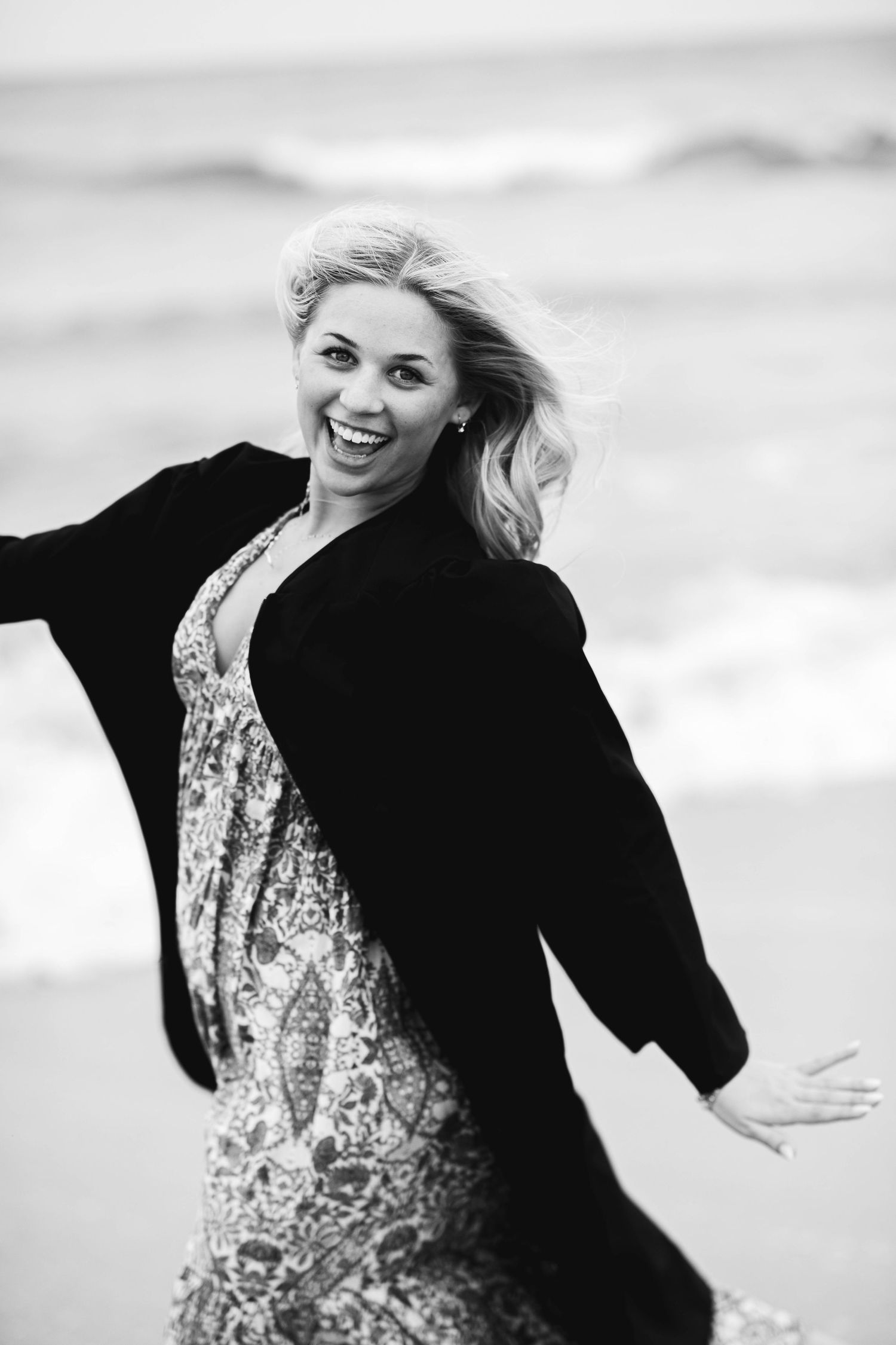 Black and white candid shot showing joyful movement in floral dress and black jacket.