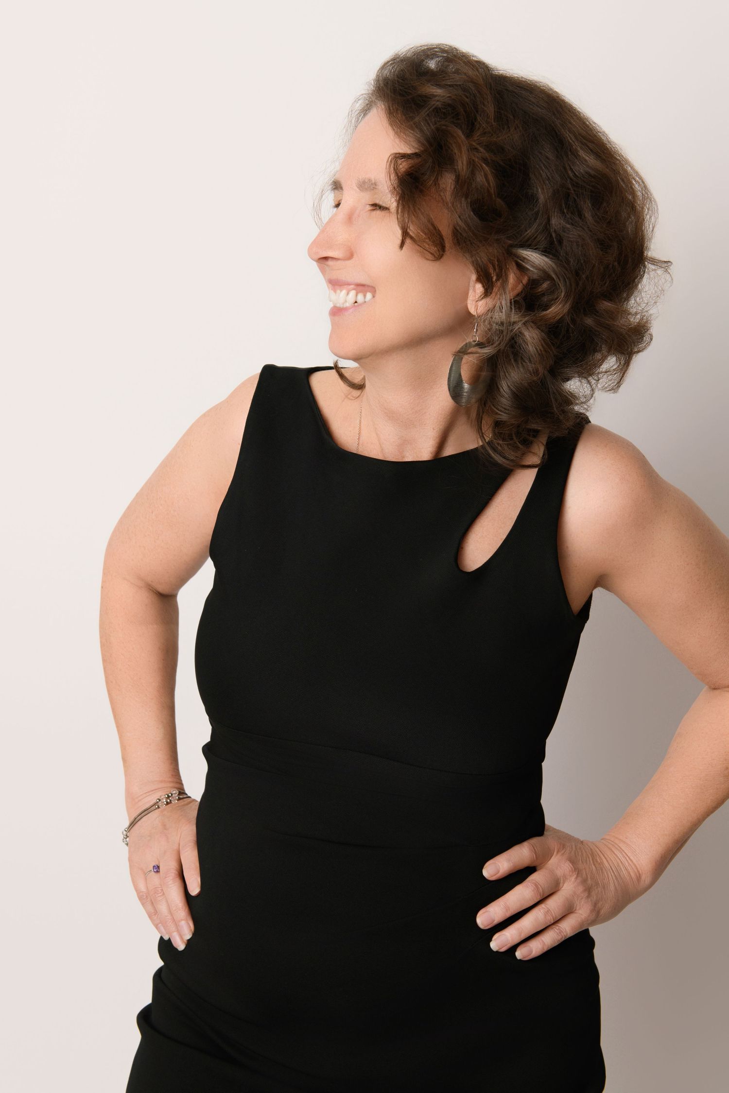 Profile portrait in black sleeveless dress with natural curls and genuine smile.