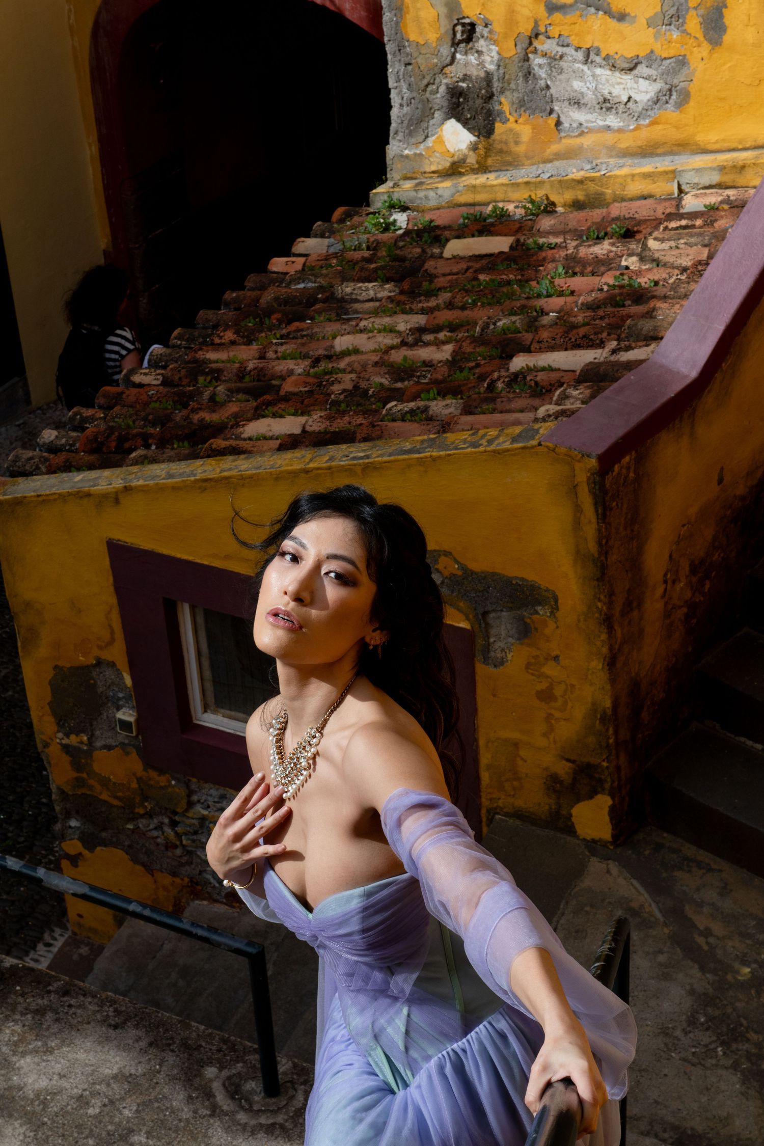 Artistic portrait against yellow weathered wall with exposed brick and purple fabric.
