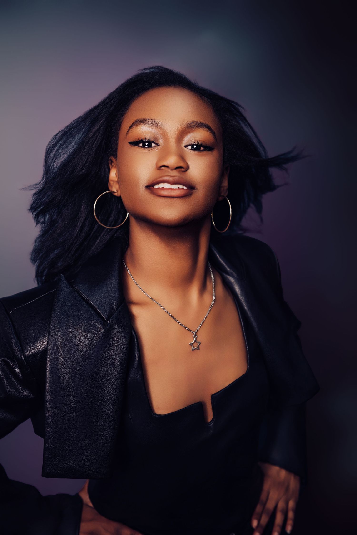 Dramatic portrait photoshoot featuring model in black jacket against dark background.