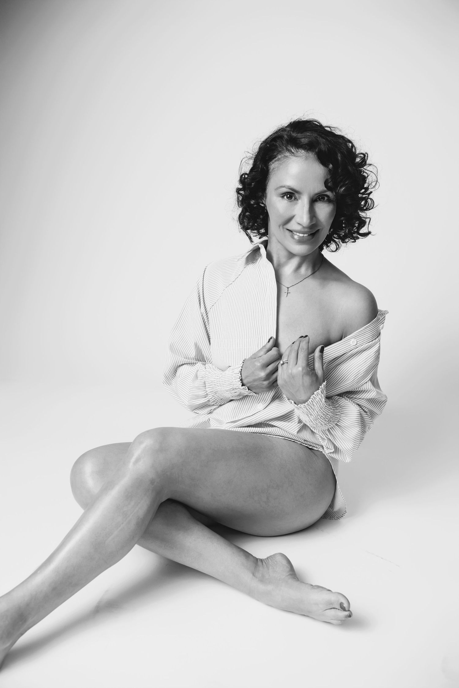 Artistic boudoir-style portrait in oversized white shirt against minimalist background.