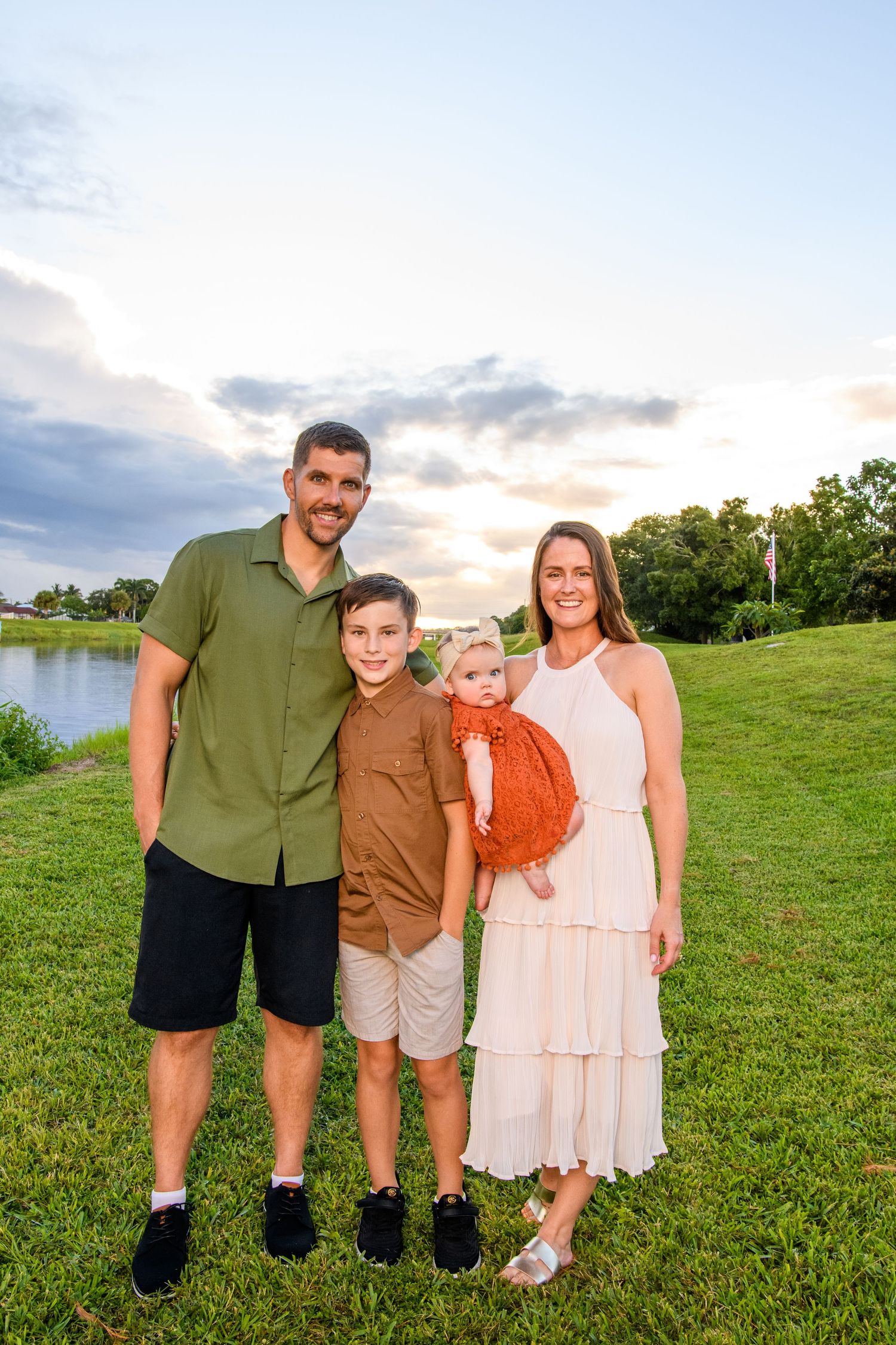Small family group standing together on green hillside at sunset.