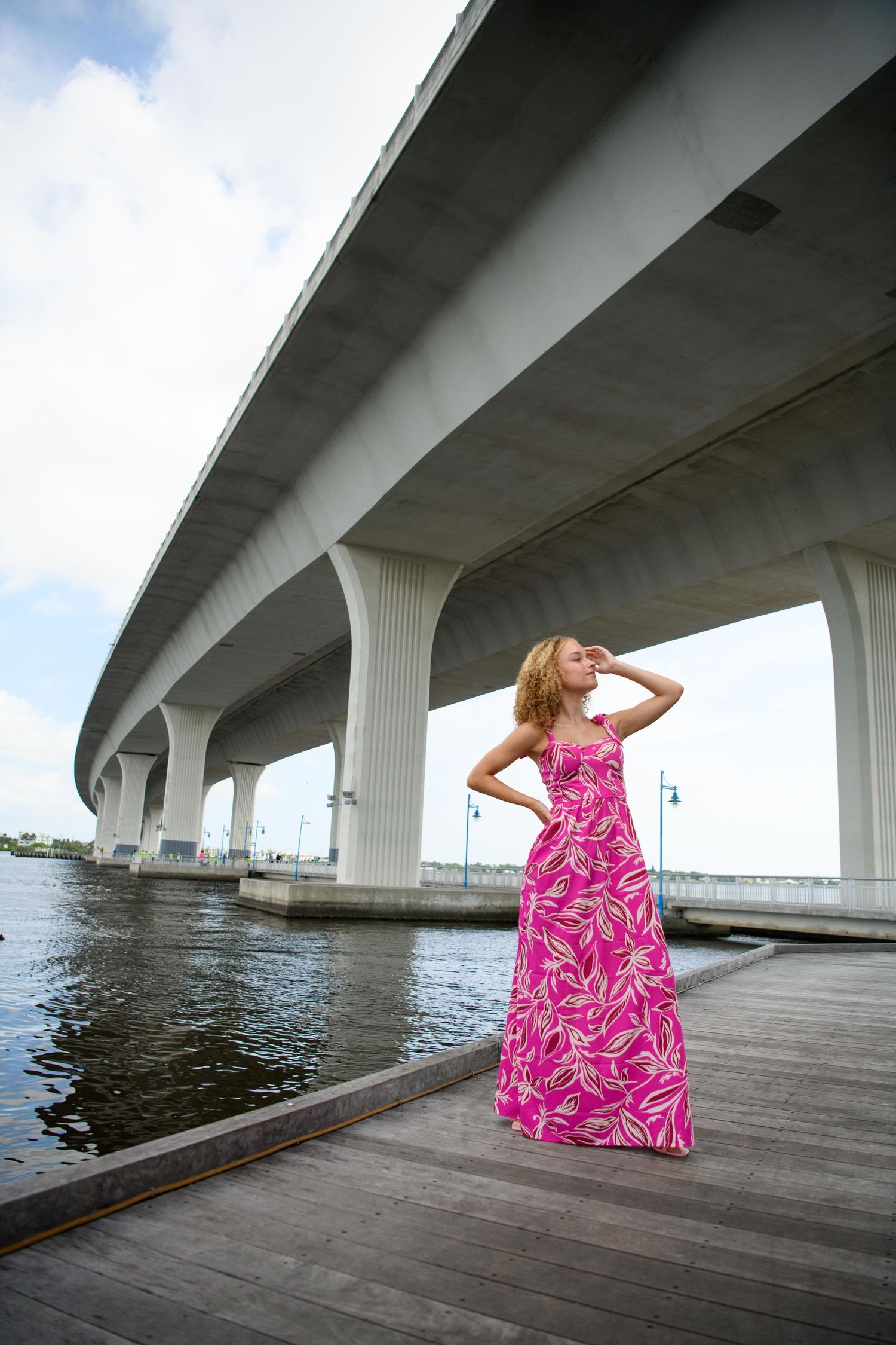 Fashion photo under bridge featuring pink floral maxi dress on wooden dock.