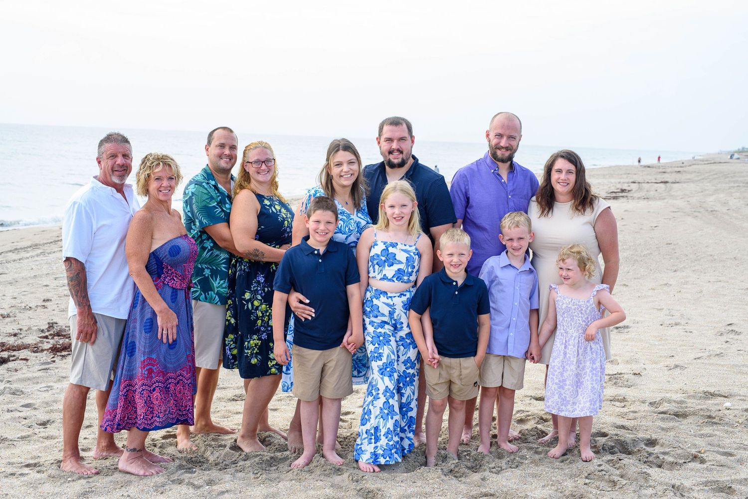 Large family group poses together on a sunny beach wearing coordinated blue and white outfits.