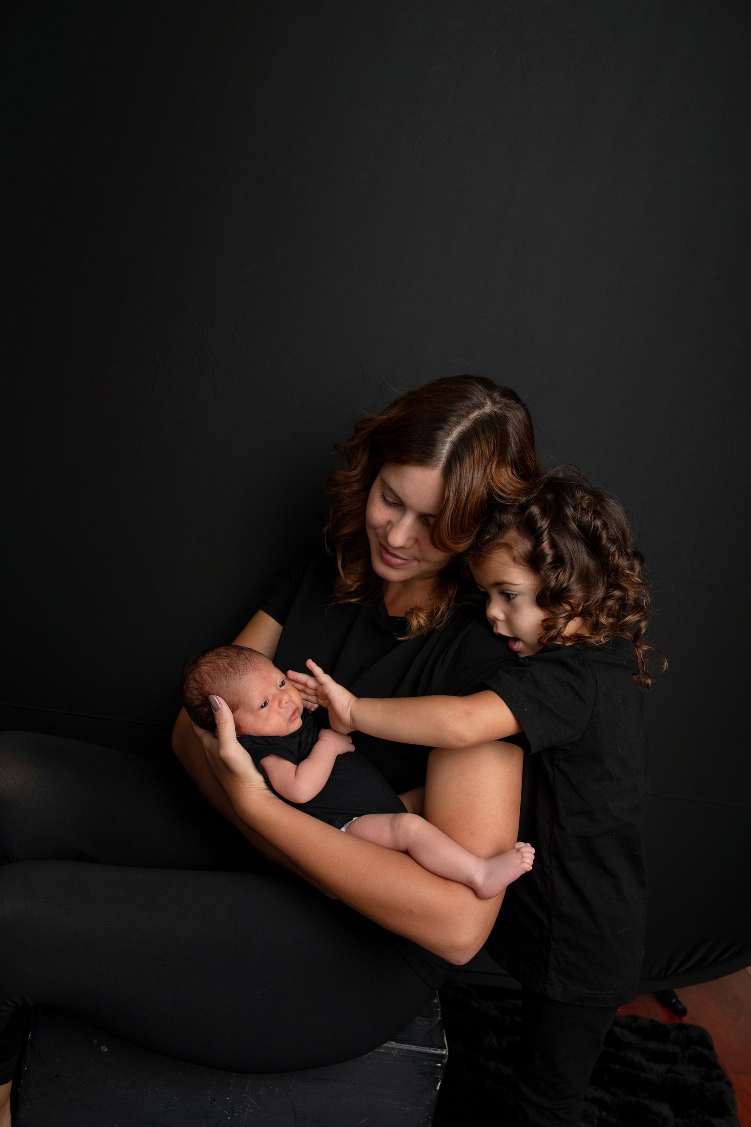 Intimate black and white portrait series showing tender moments between parent and children against dark backdrop.