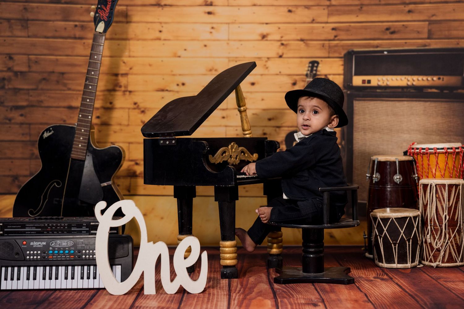 Collection of musical instruments including piano and drums against wooden wall backdrop.