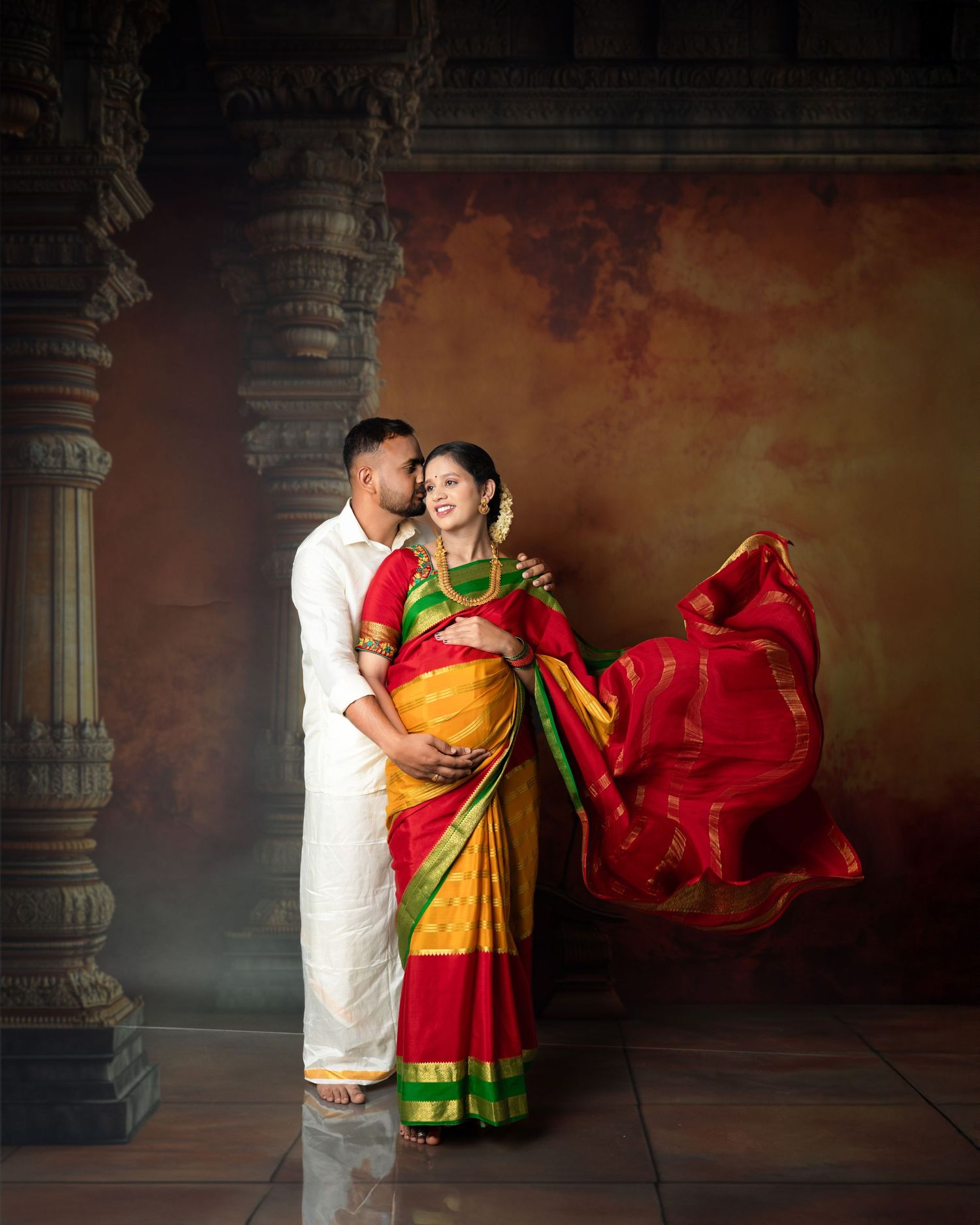 Artistic wedding portrait with flowing red saree against rustic temple backdrop.