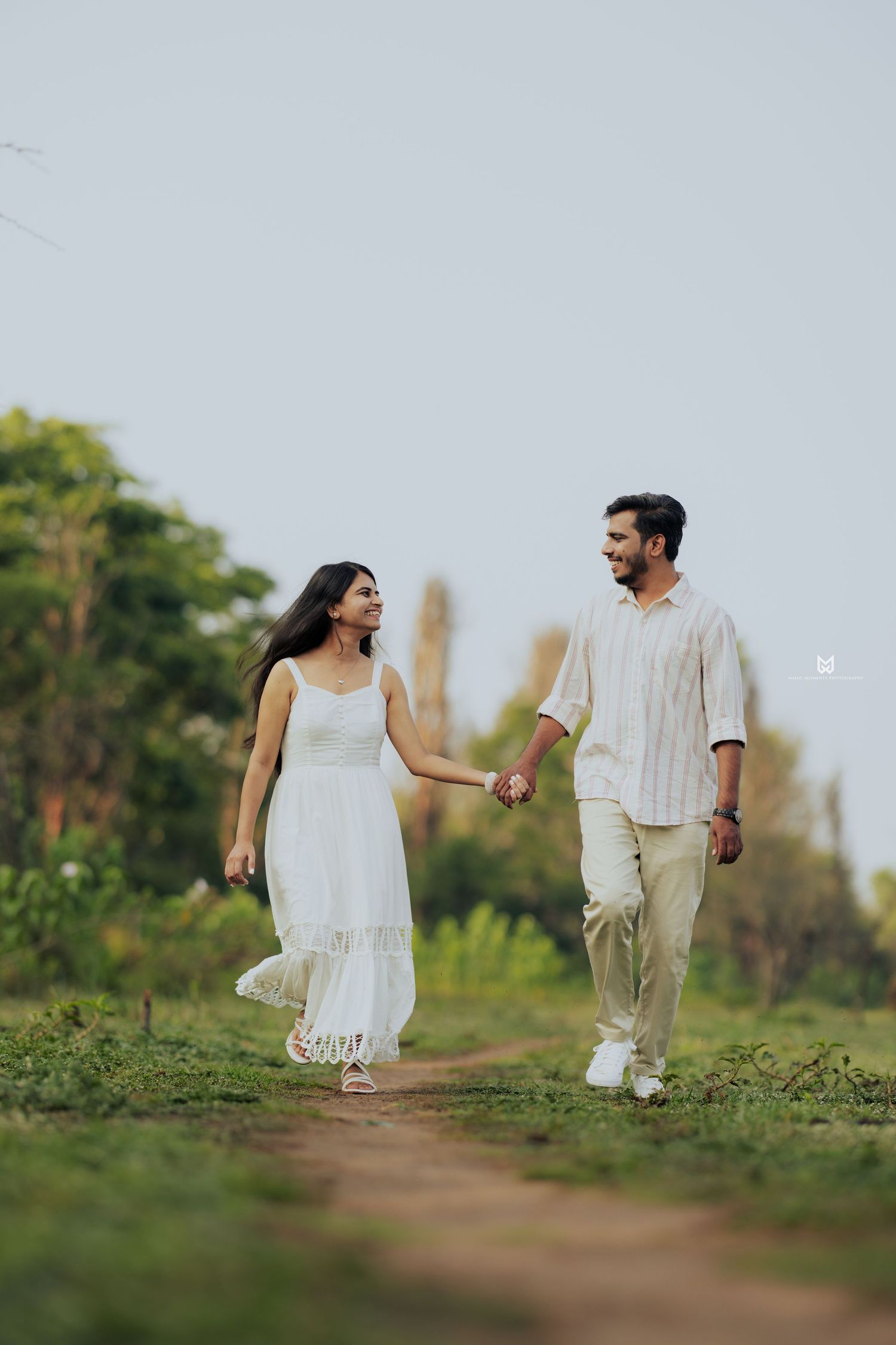 Couple in white outfits walking together on a grassy path during sunset.