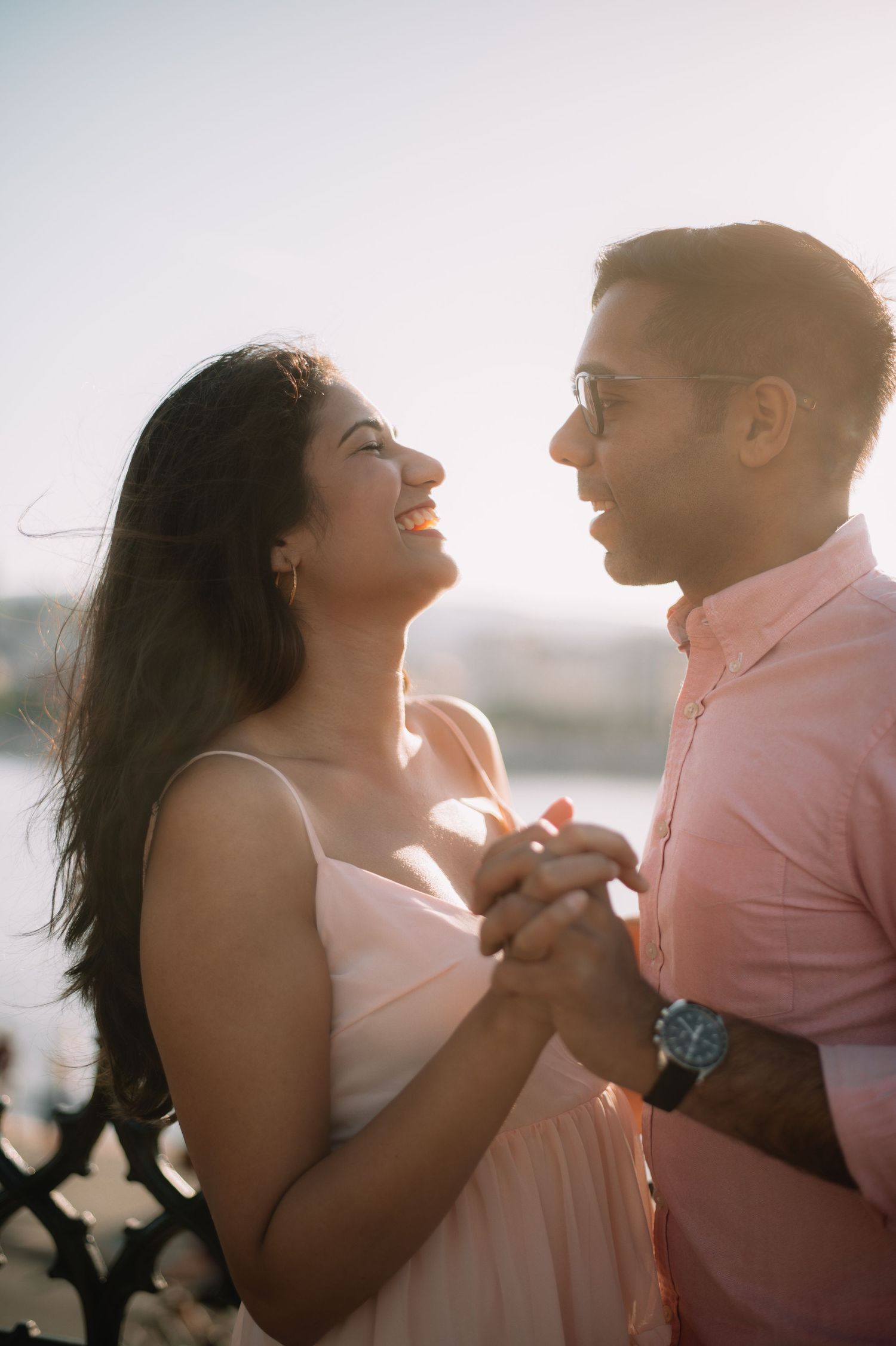 A joyful couple holds hands and gazes at each other in golden sunset light outdoors.