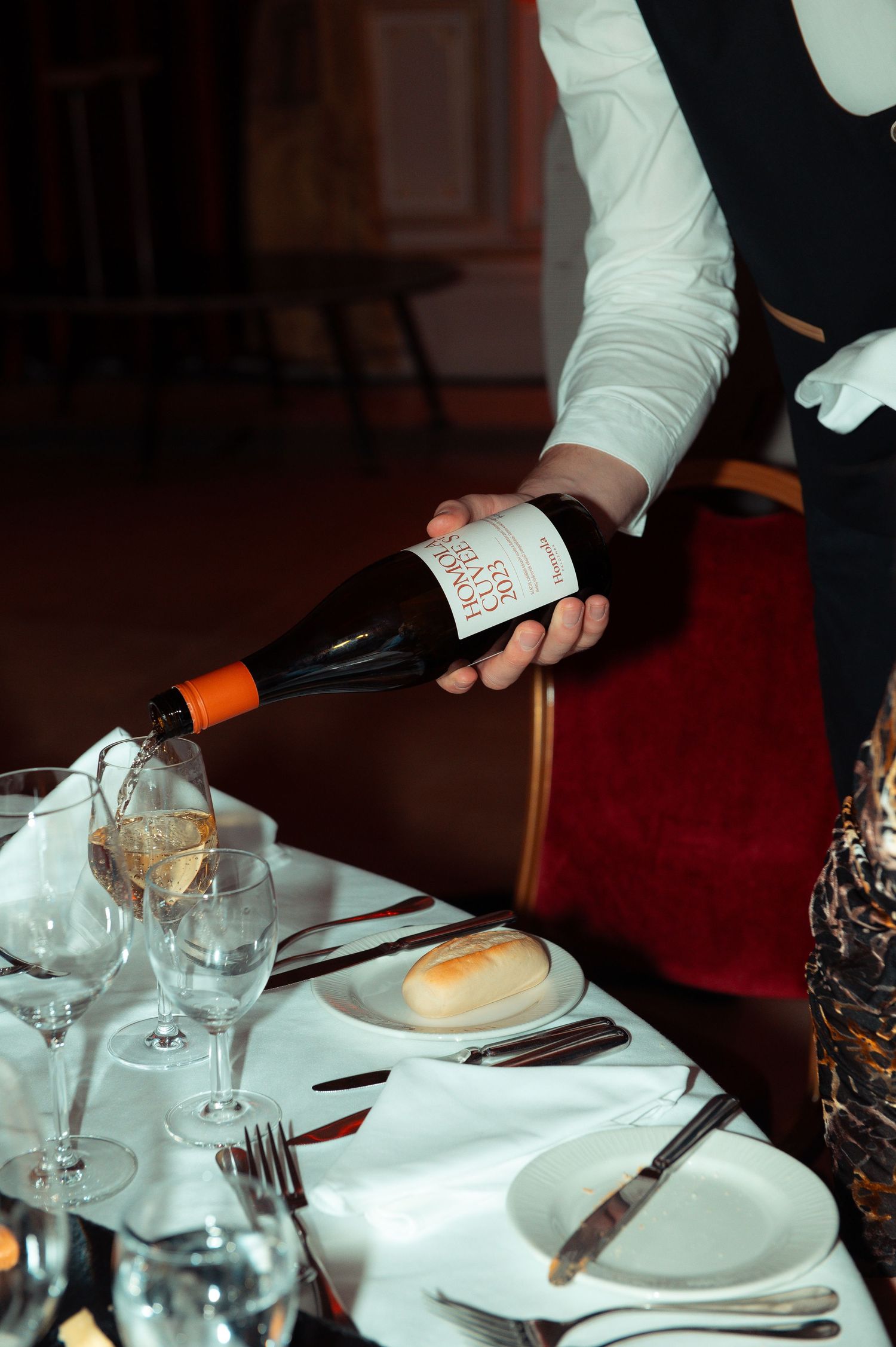 Elegant waiter pouring white wine at a fine dining table set with crystal glasses and white linen.