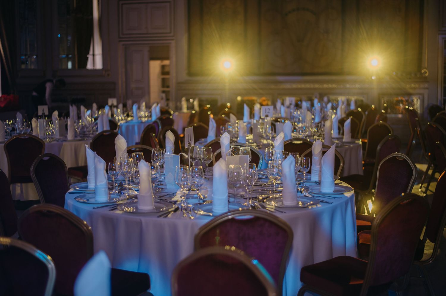 Elegant banquet hall with round tables set for a formal dinner, featuring white linens, glassware, and candlelight.