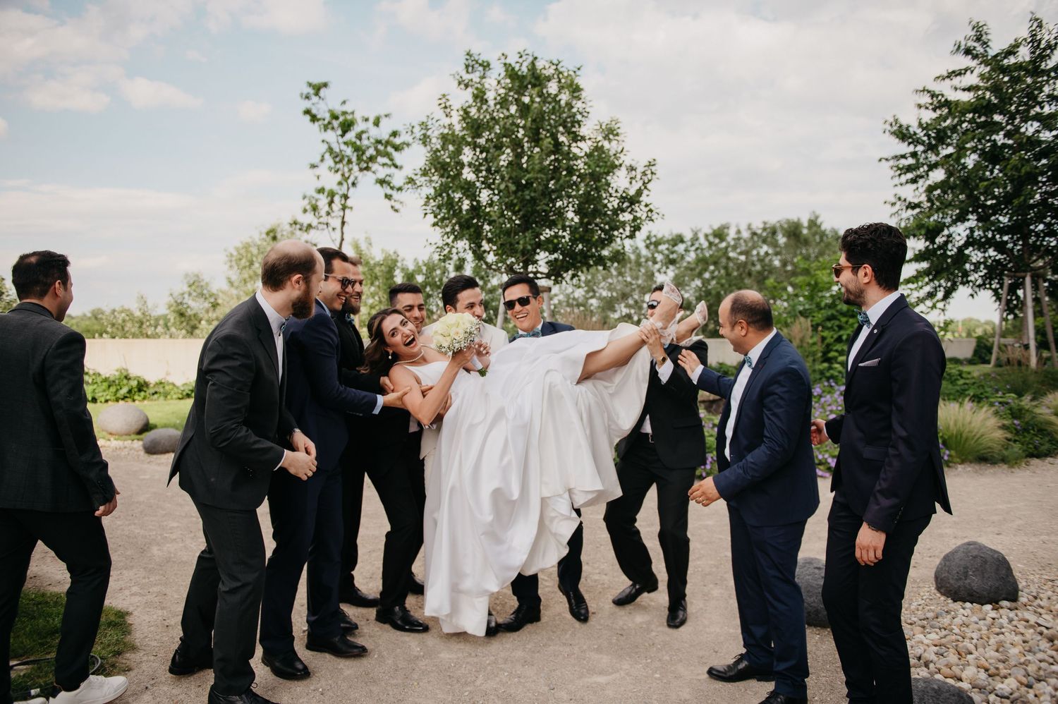 Groom carried by groomsmen in suits during fun outdoor wedding celebration photo.
