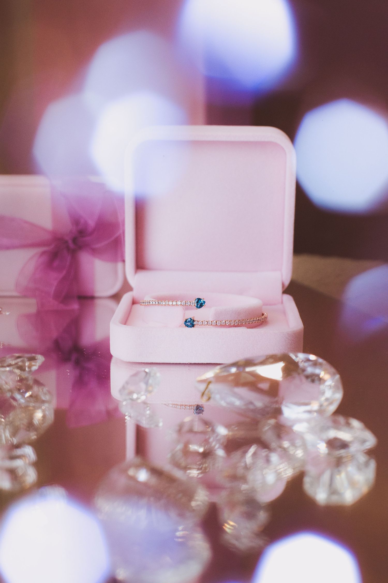 A delicate blue gemstone ring displayed in an open pink velvet jewelry box surrounded by crystal decorations.