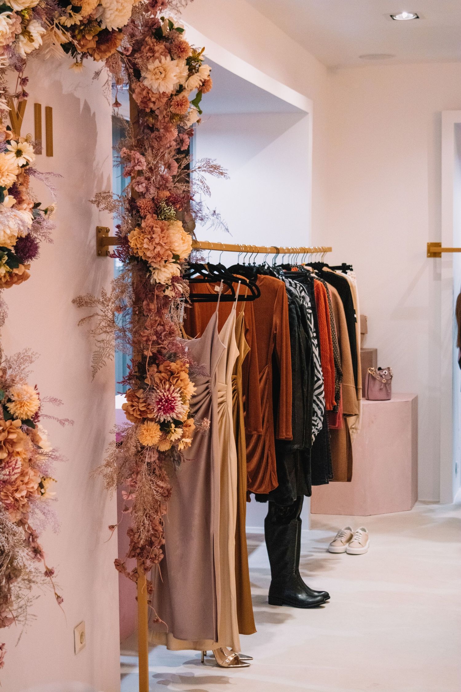 Elegant boutique interior with floral arch decoration and clothing rack featuring autumn-toned dresses.