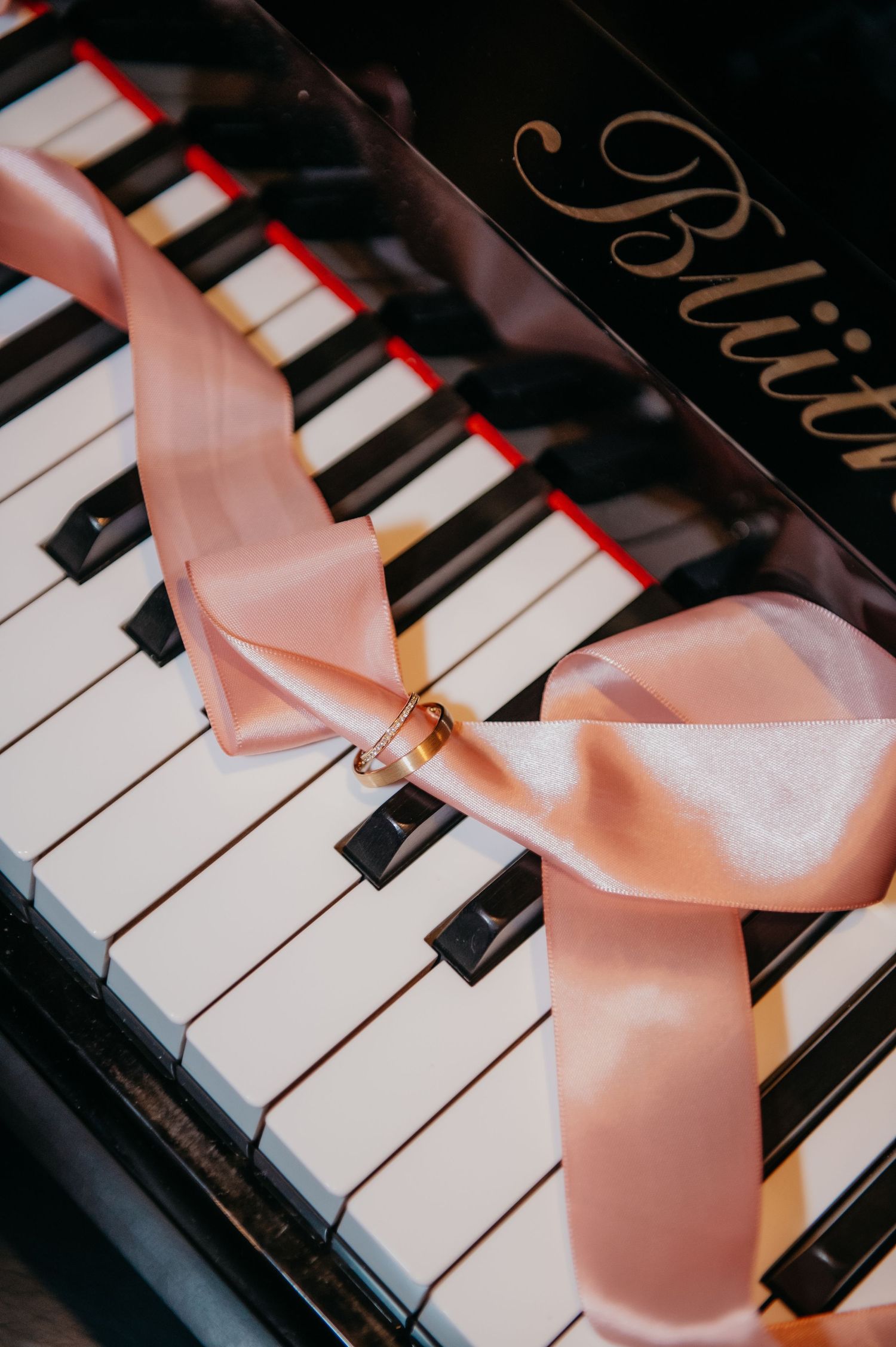 Wedding rings tied with pink satin ribbon on Blüthner grand piano keys.