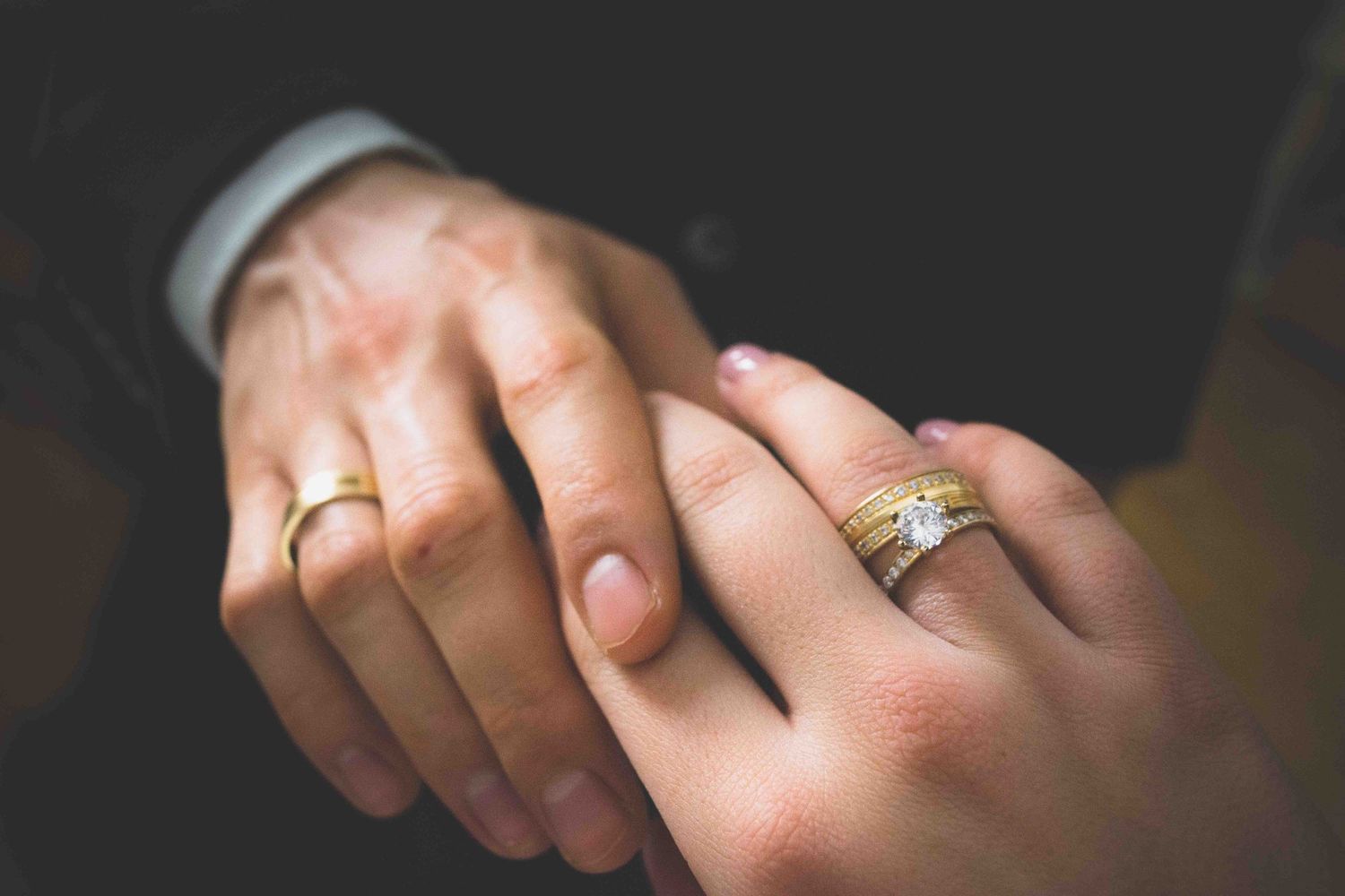 Close-up of newlywed couple holding hands showing gold wedding bands and diamond engagement ring.