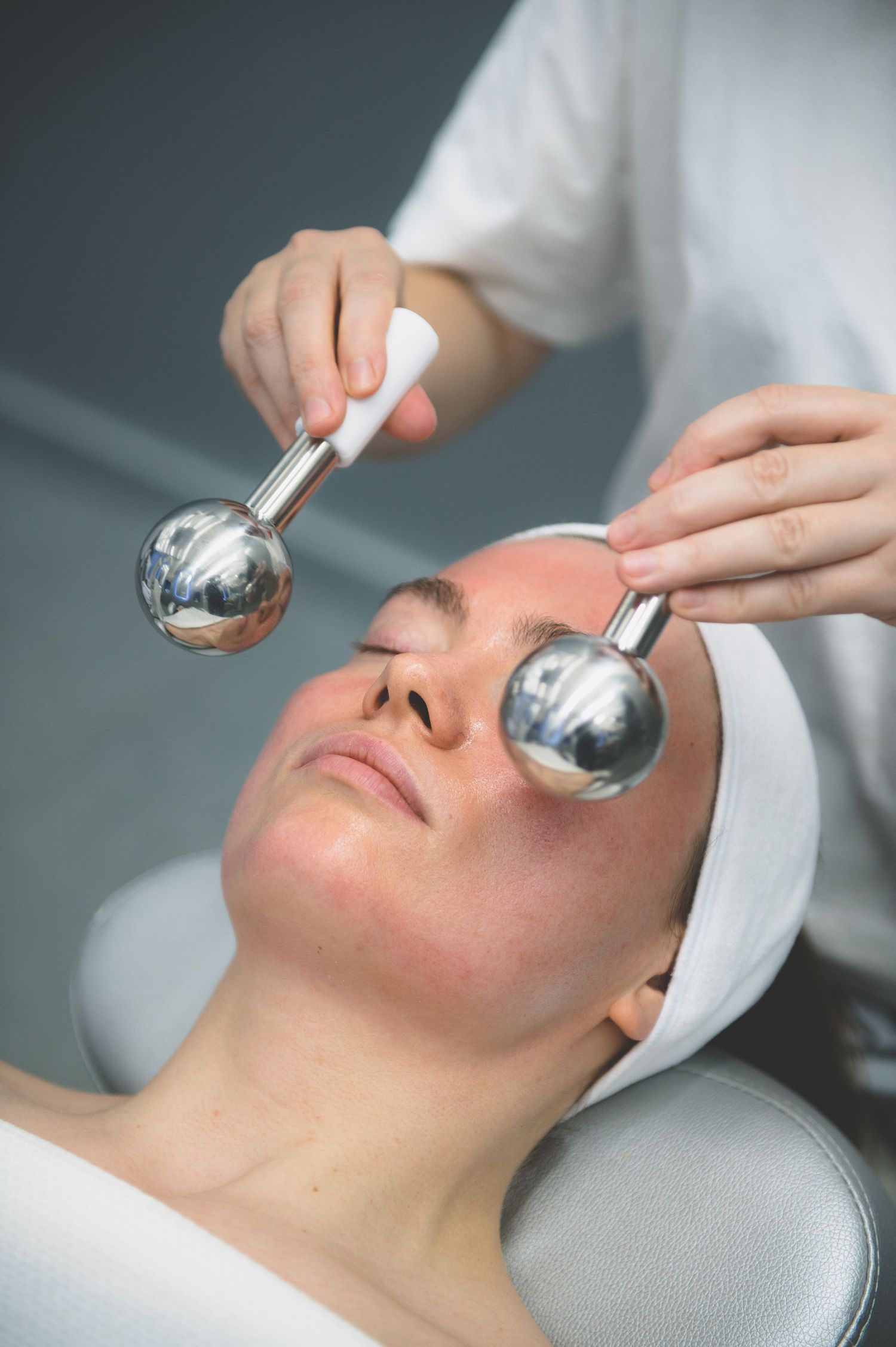 Esthetician applying silver cryo globes facial massage tools to a woman's face during a spa treatment.