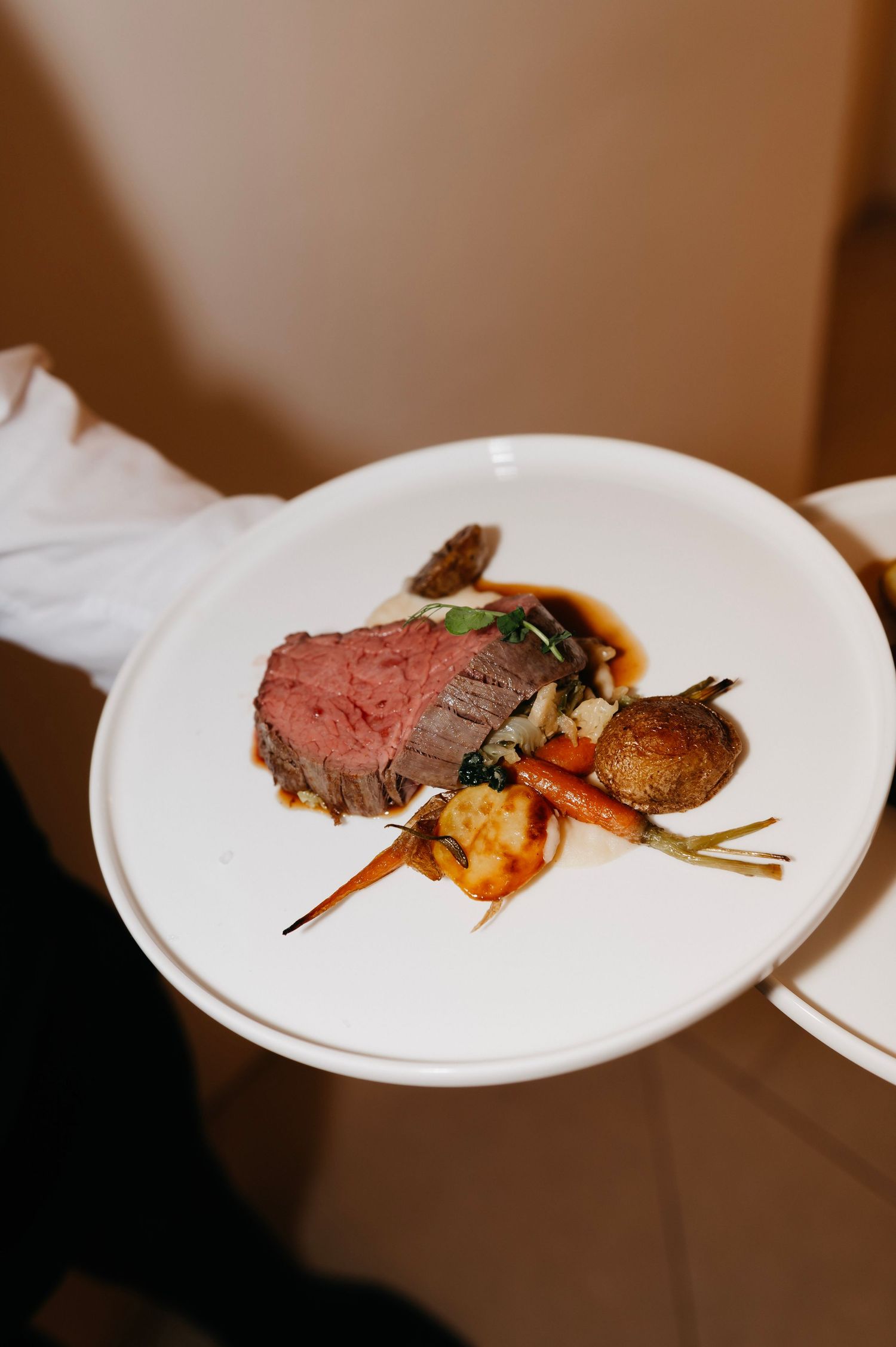 Elegant plated beef tenderloin with roasted carrots, mushroom, and rich sauce served on a white plate.