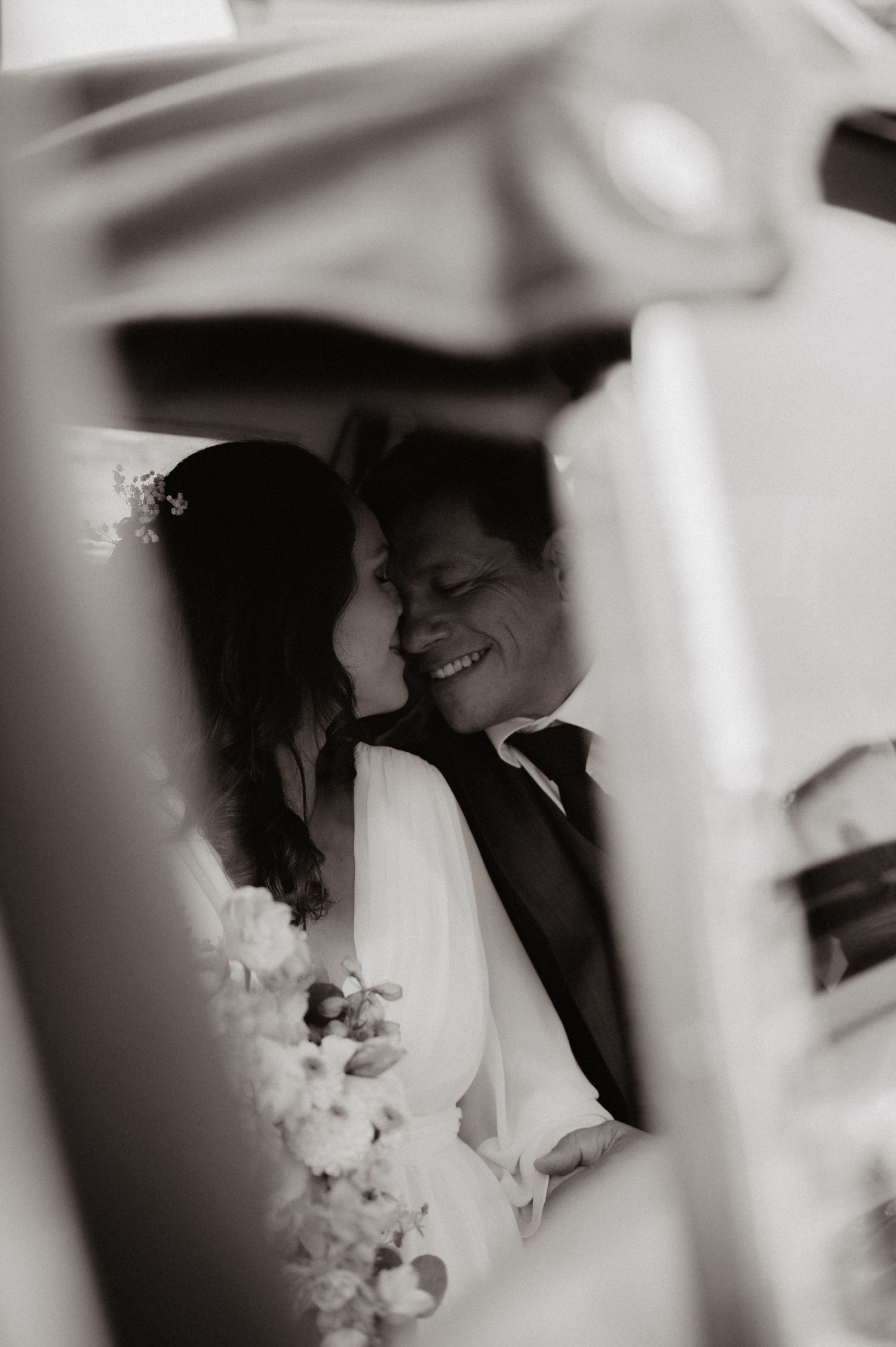 Bride and groom smiling together through a white architectural frame in romantic black and white wedding photography.