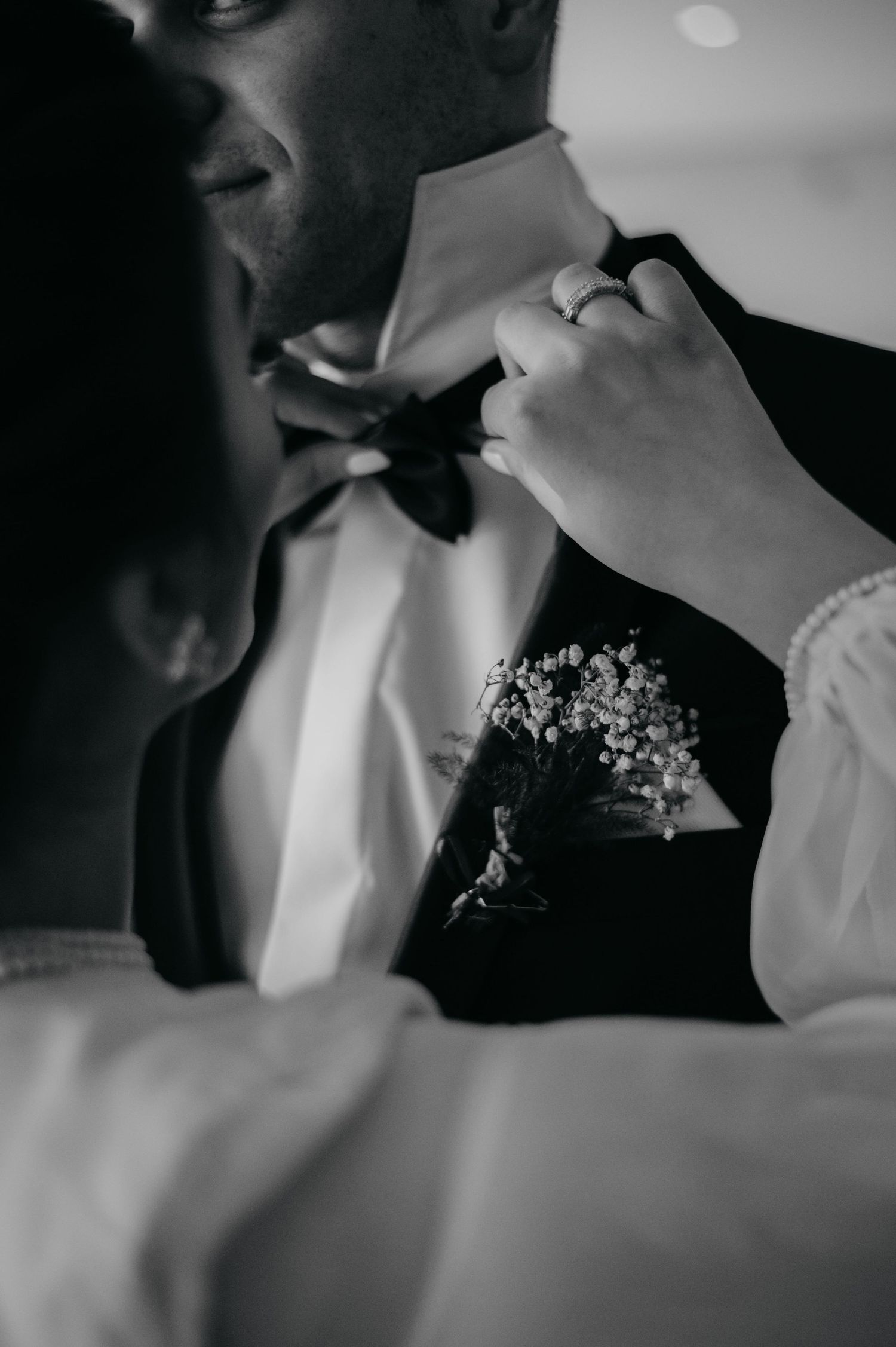 Black and white close-up of bride adjusting grooms bow tie with wedding ring visible.