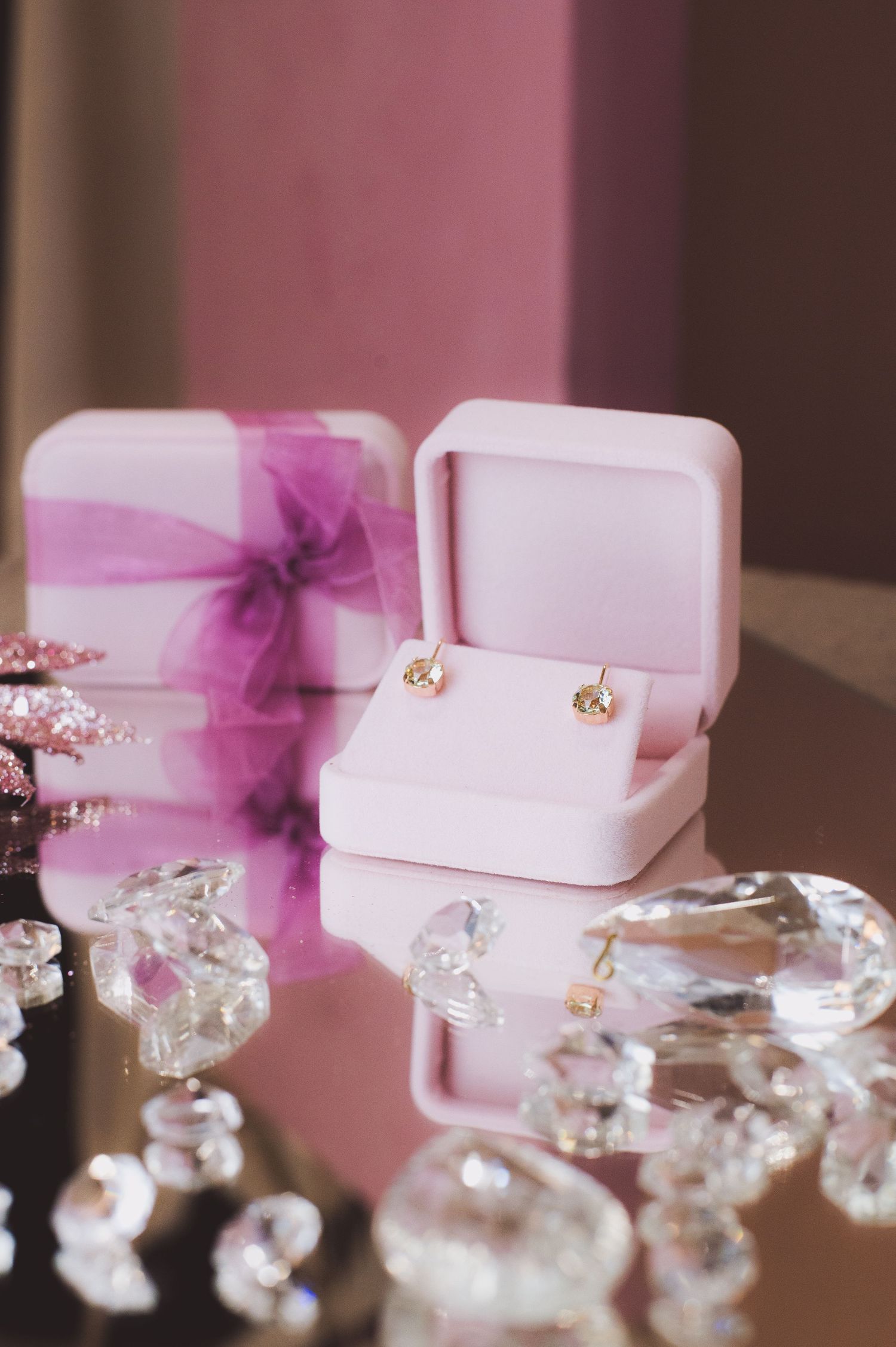 Gold stud earrings displayed in a pink velvet jewelry box surrounded by crystal diamonds and a pink gift box.