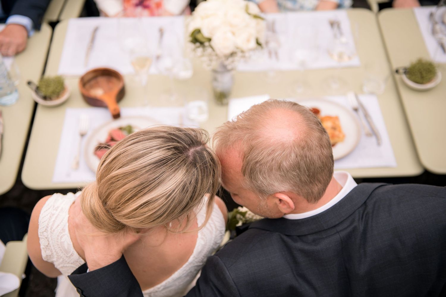 Aerial view of bride and groom sharing intimate moment while leaning heads together at reception table.