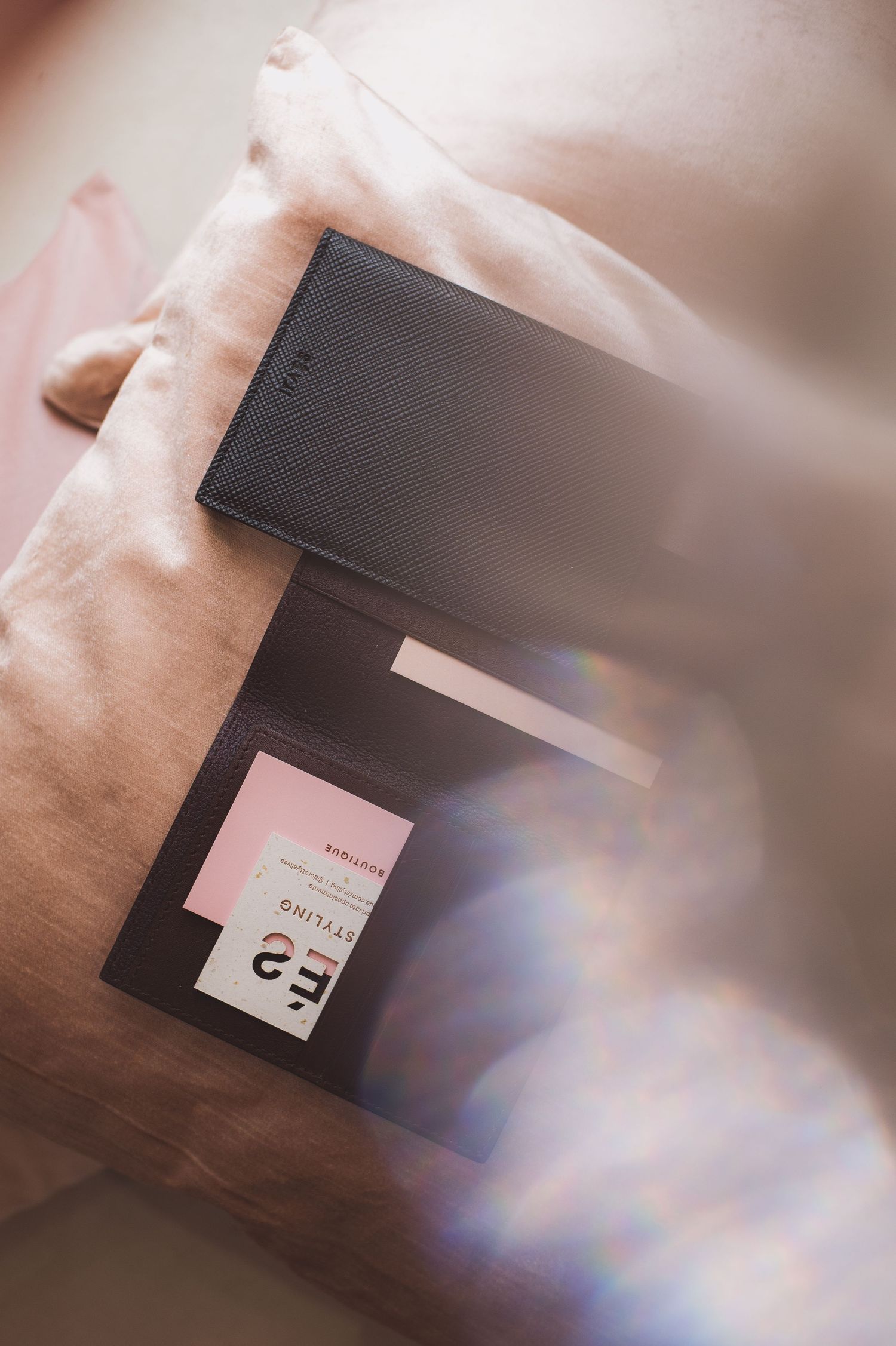 Black leather card holder wallet open showing business cards, placed on a light pink fabric surface.