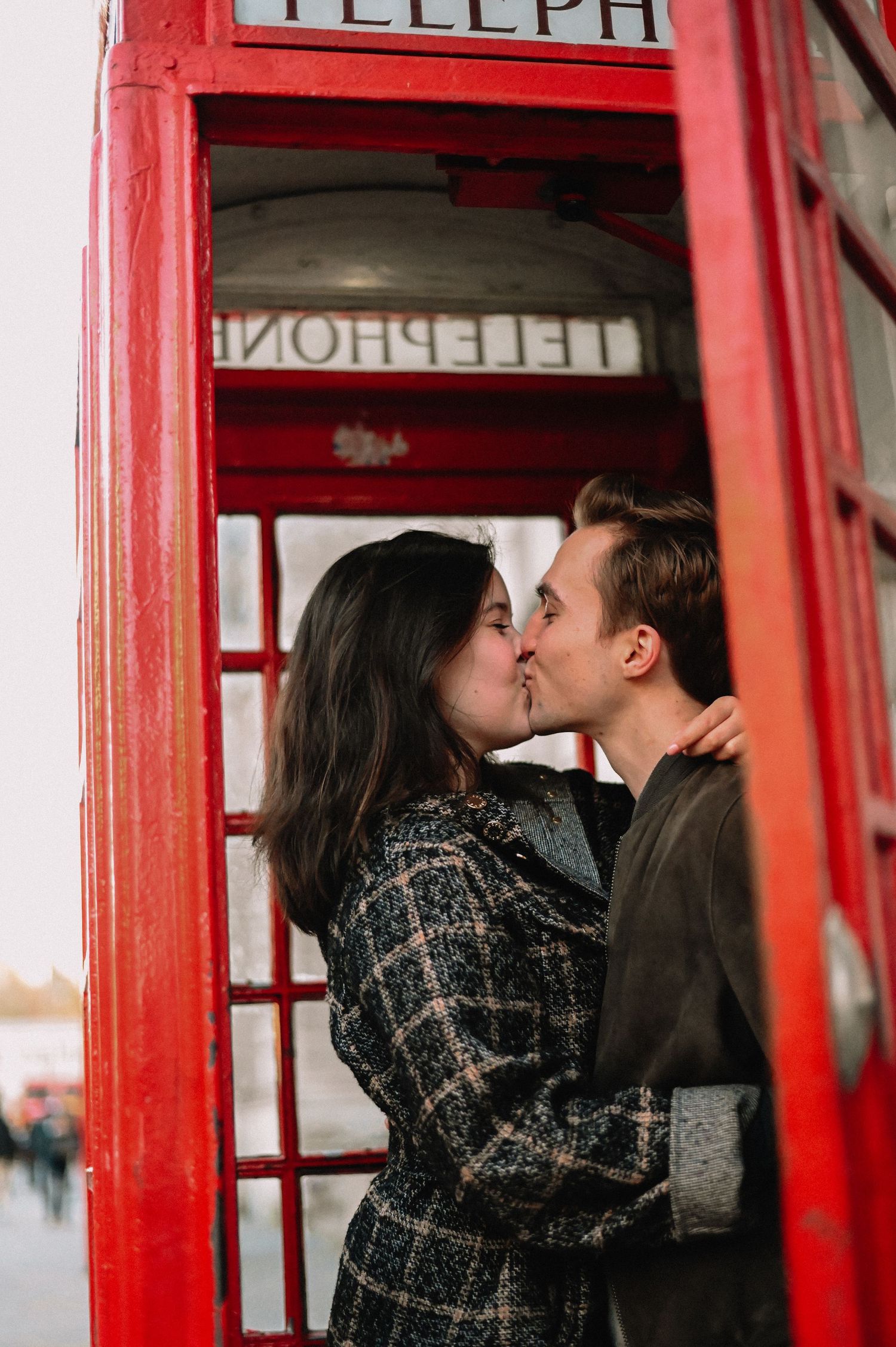 Couple sharing a romantic kiss beside a classic red British telephone box in London.