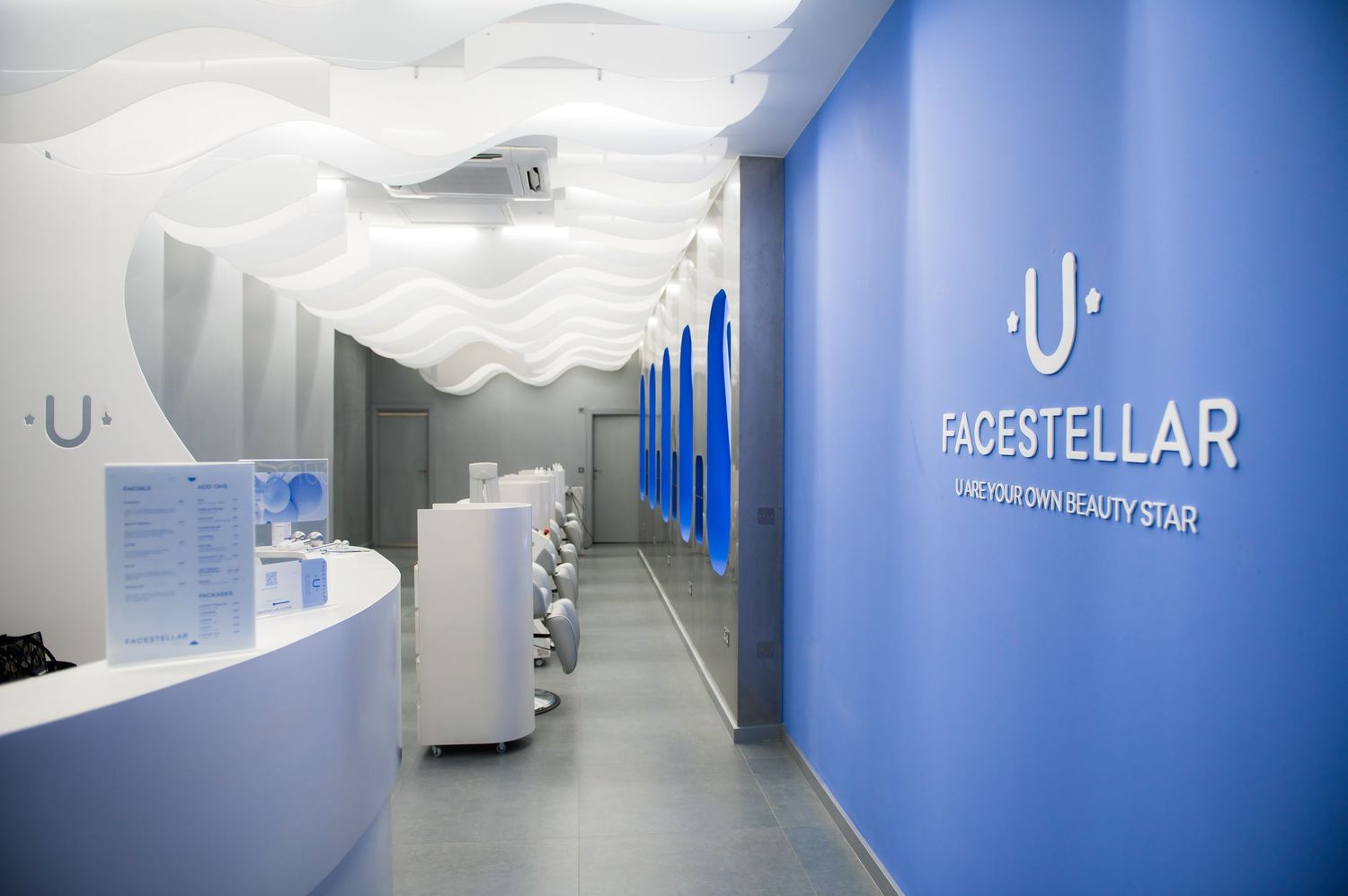 Modern Facestellar beauty store interior with white wave ceiling, blue accent wall, and sleek white reception desk.
