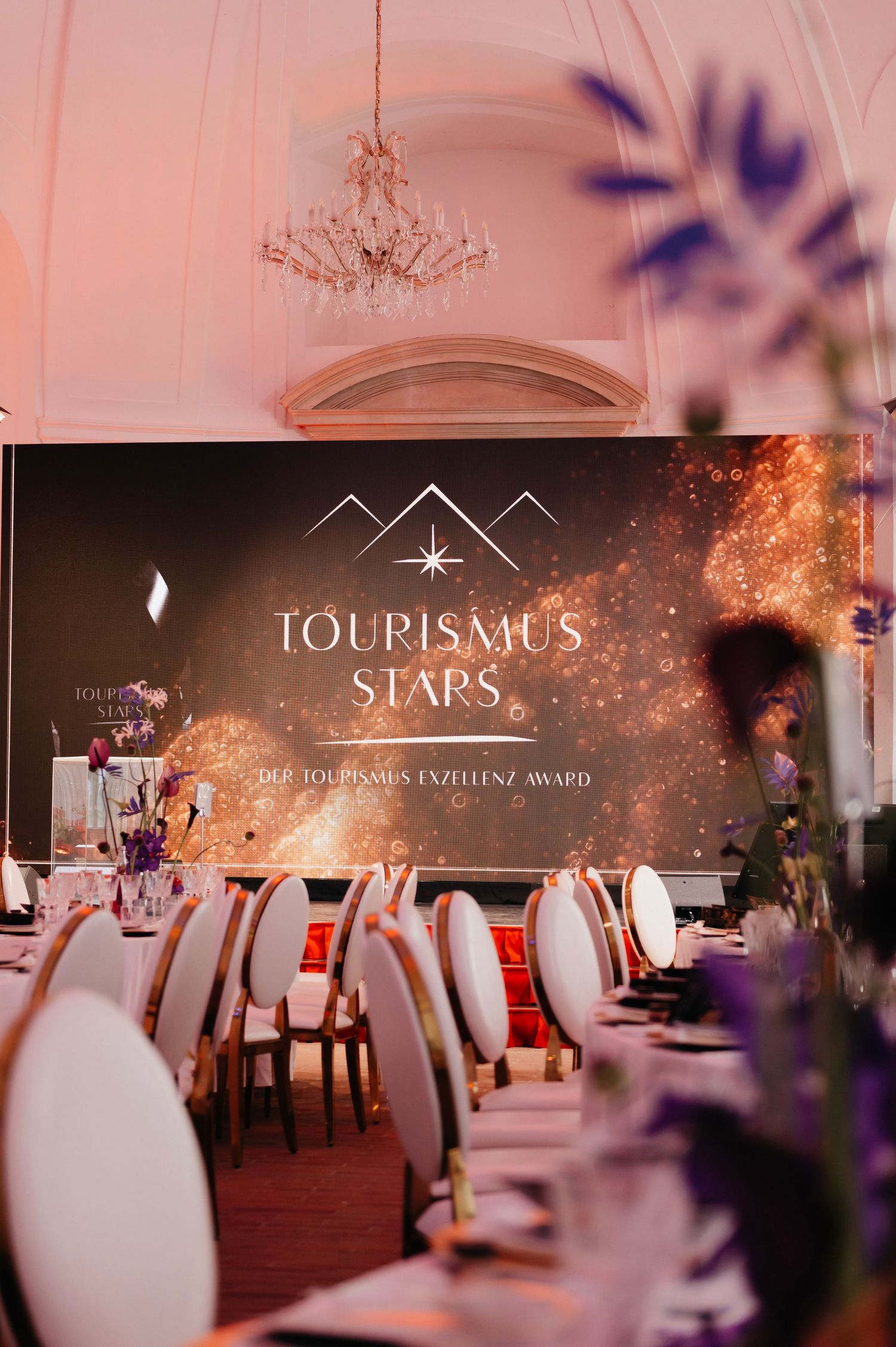 Elegant Tourismus Stars award ceremony venue with white chairs, floral arrangements, and a glowing backdrop display.